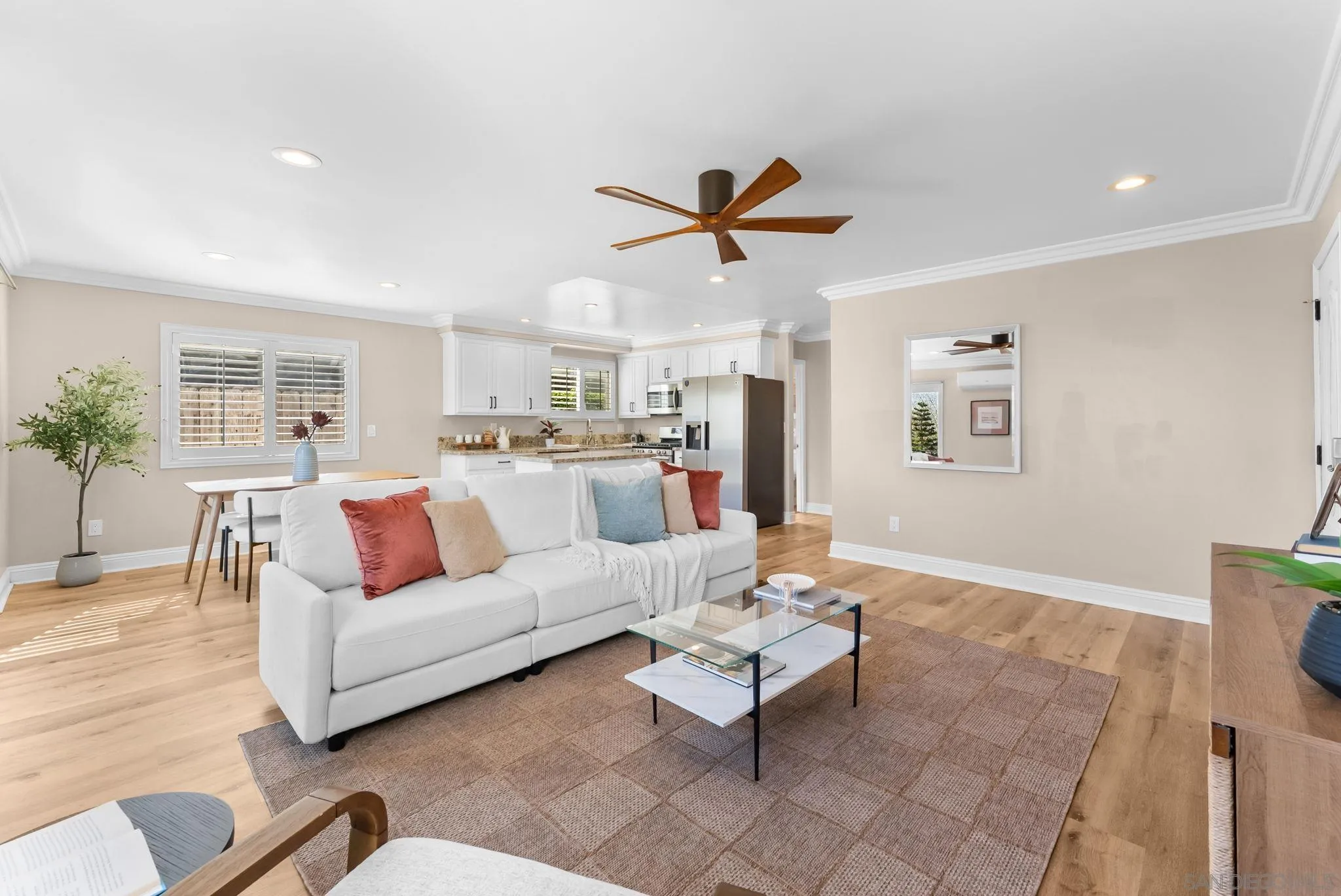 Staged living room opening to a white-cabinet kitchen, with a white sofa and warm wood floors.