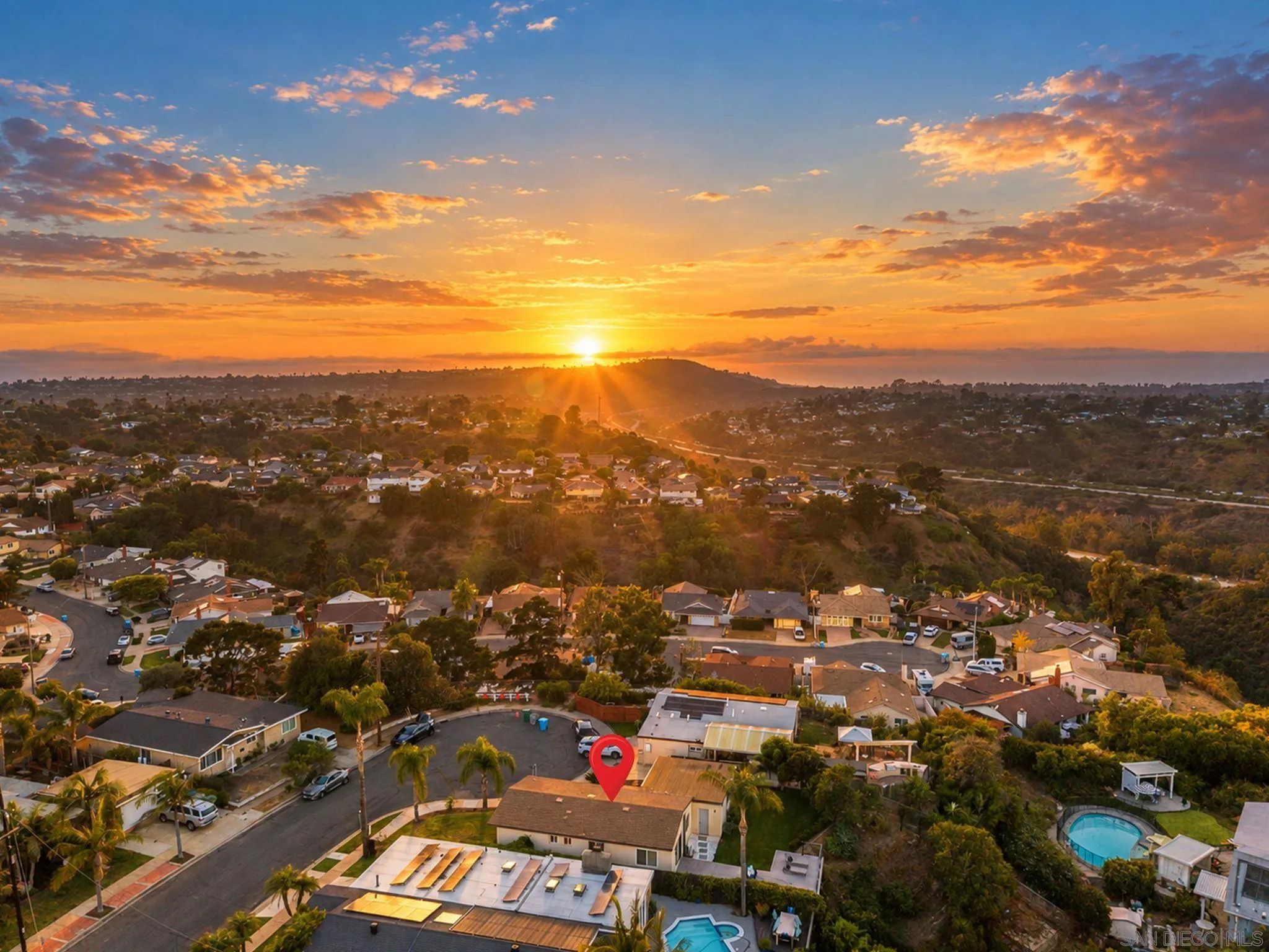 Aerial neighborhood view at sunset, with a red map pin marking a home among palm-lined streets.