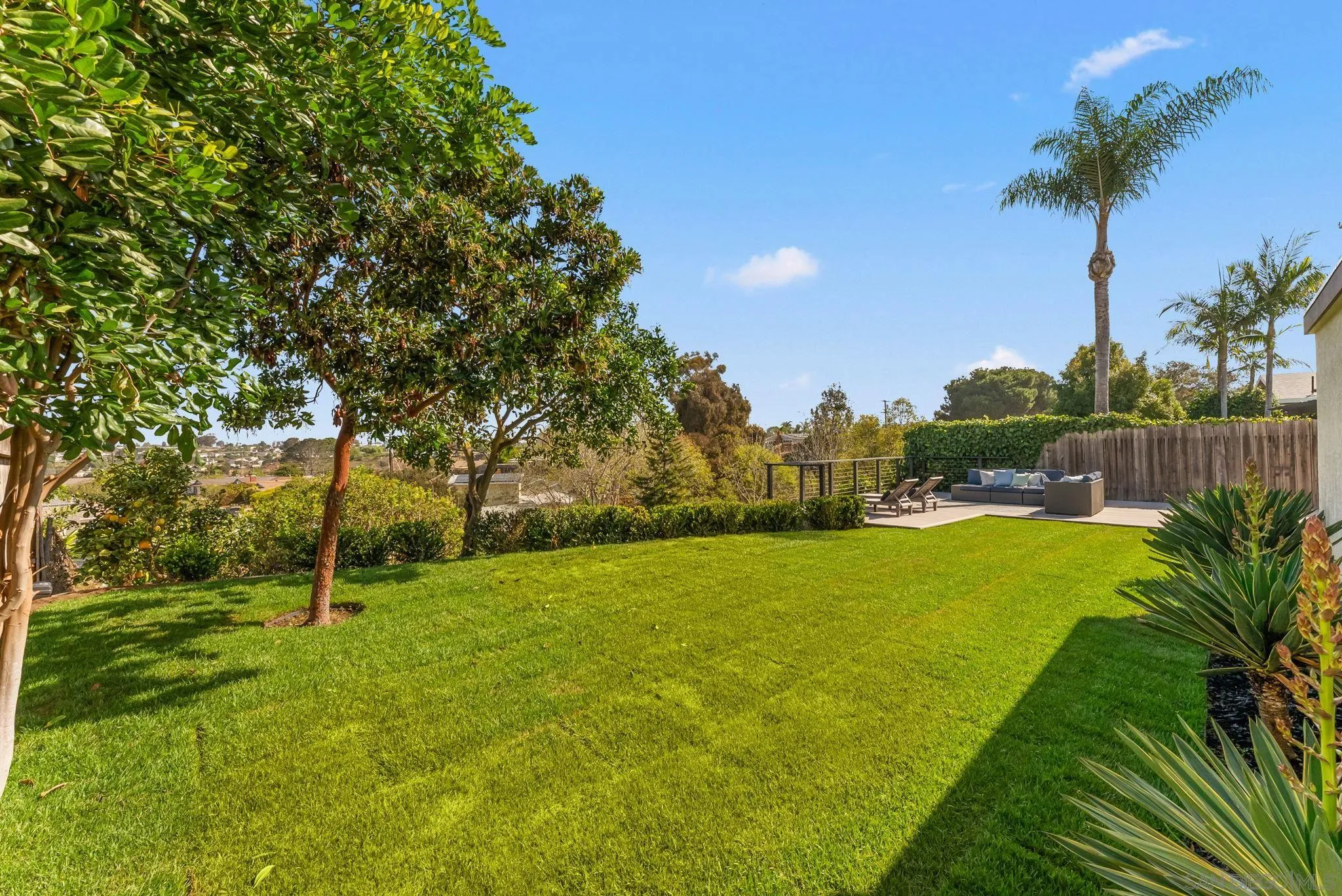 Landscaped backyard with a broad lawn, mature trees, and a furnished patio overlooking the neighborhood.