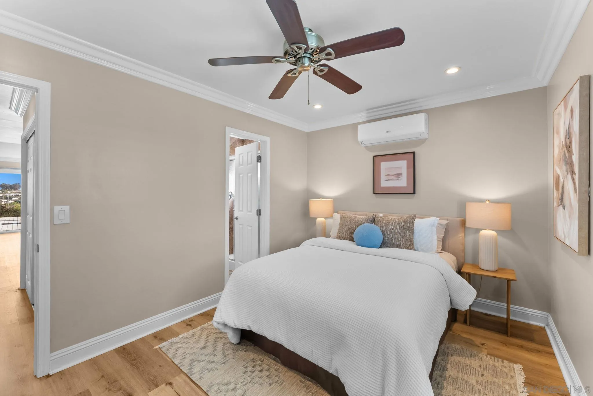 Staged bedroom with a white bed, ceiling fan, and wall-mounted air conditioner.