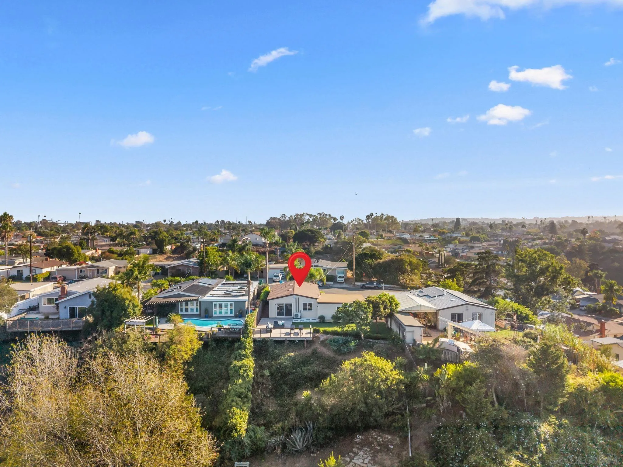 Aerial view of the home marked by a red pin, with nearby houses and a steep, tree-covered hillside.