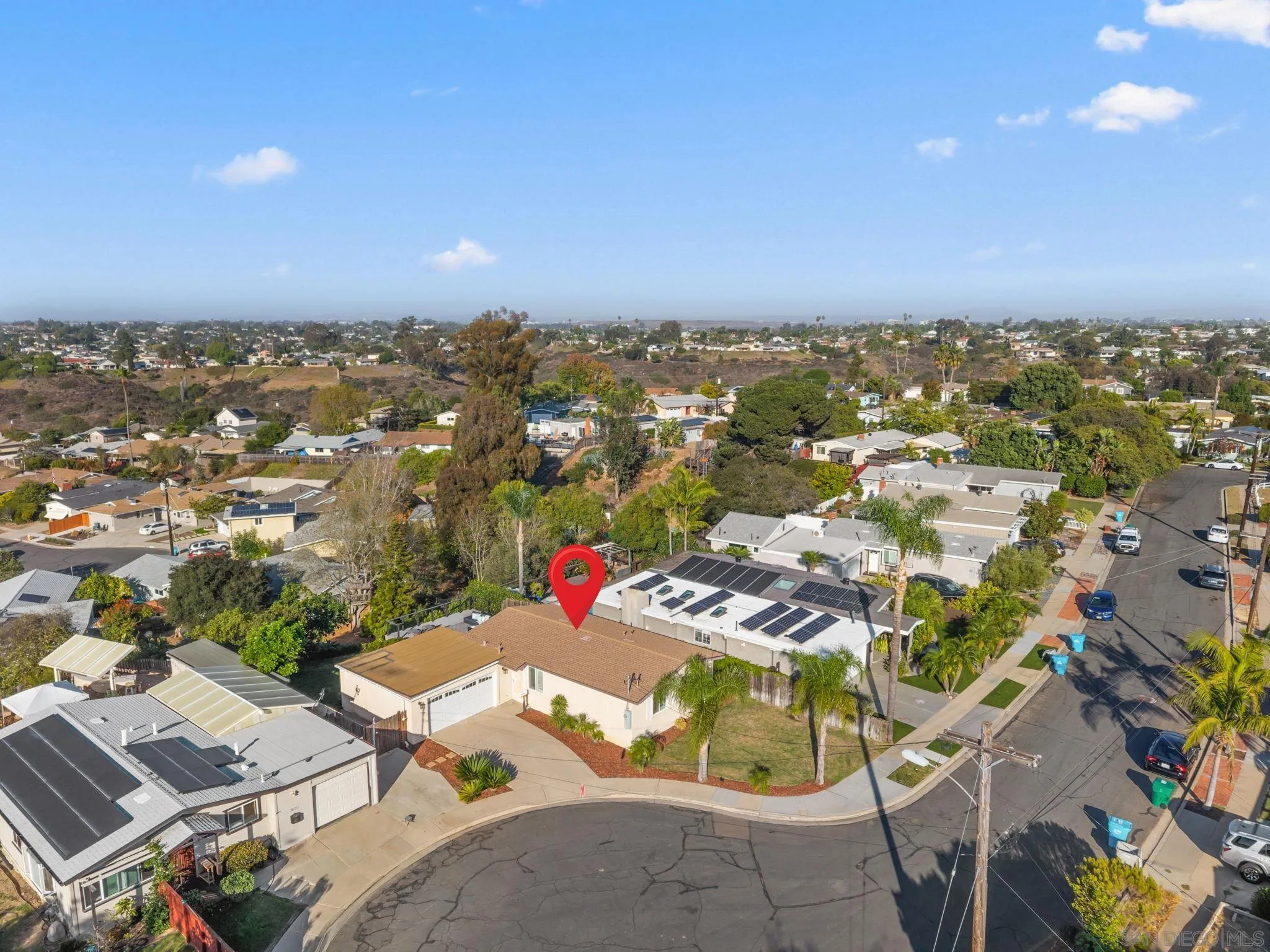 Aerial view of a corner-lot home marked by a red pin, with neighboring homes and solar-panel rooftops.