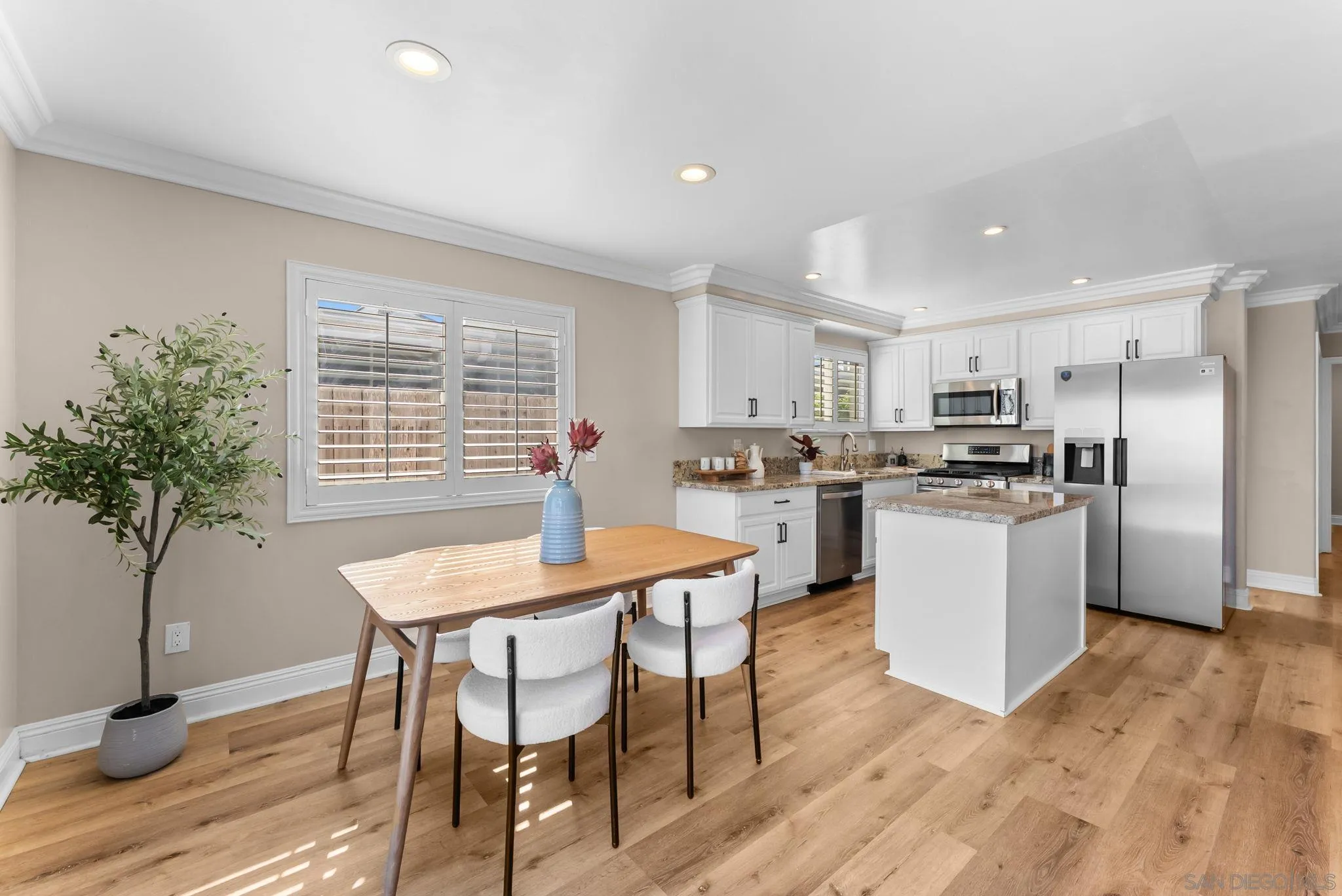 Staged kitchen with white cabinets, stainless steel appliances, an island, and a wood dining table.