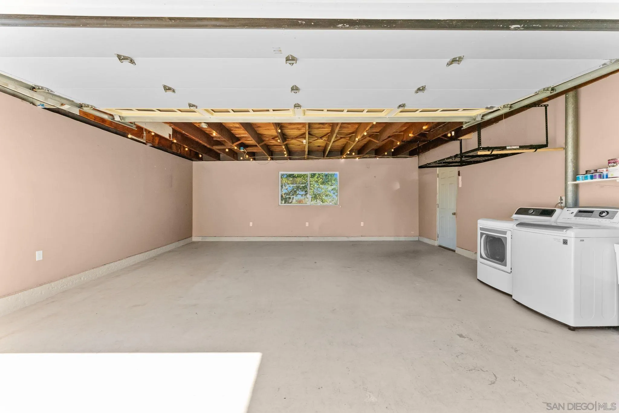 Spacious garage with exposed ceiling framing, open overhead door, and washer and dryer.