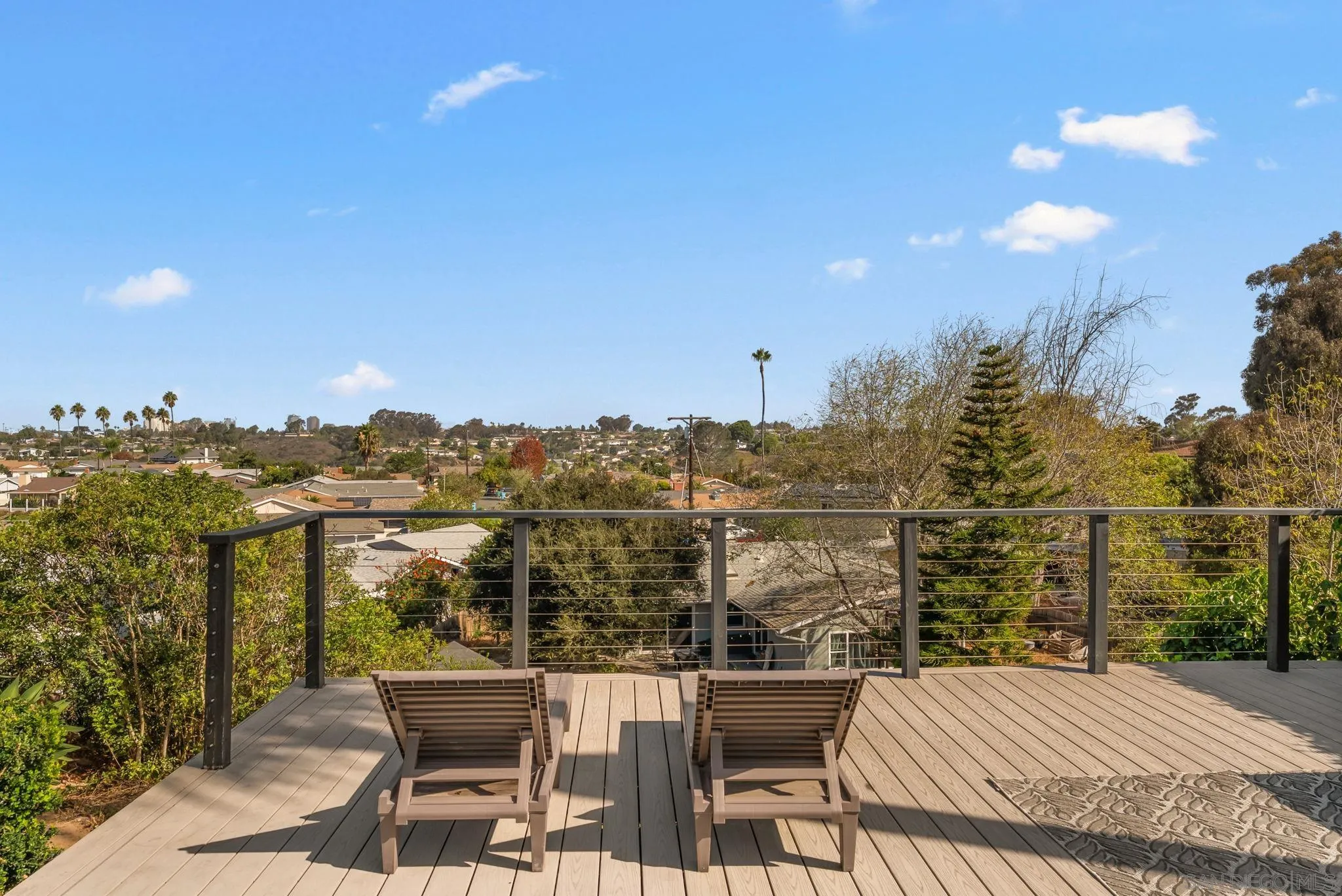 Wood deck with lounge chairs and cable railing overlooking a leafy neighborhood.