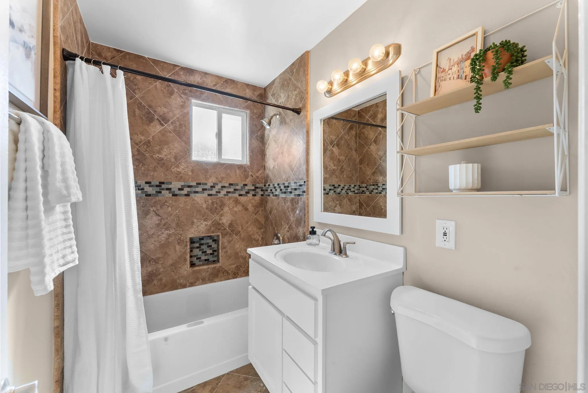 Bathroom with brown tile tub surround, white vanity and toilet, and open wall shelving.