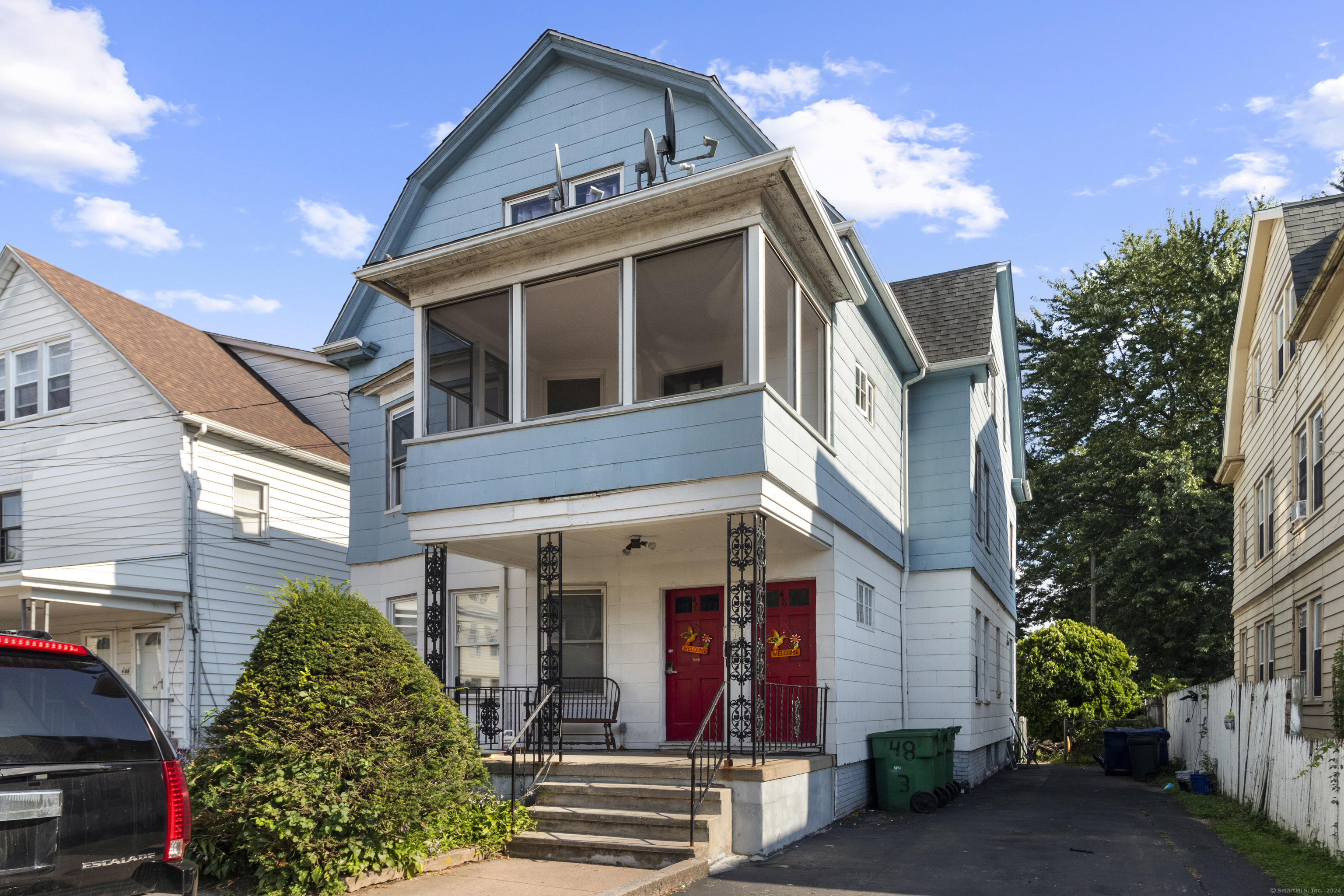 Blue multi-story house with an enclosed porch, two red front doors, and front steps.
