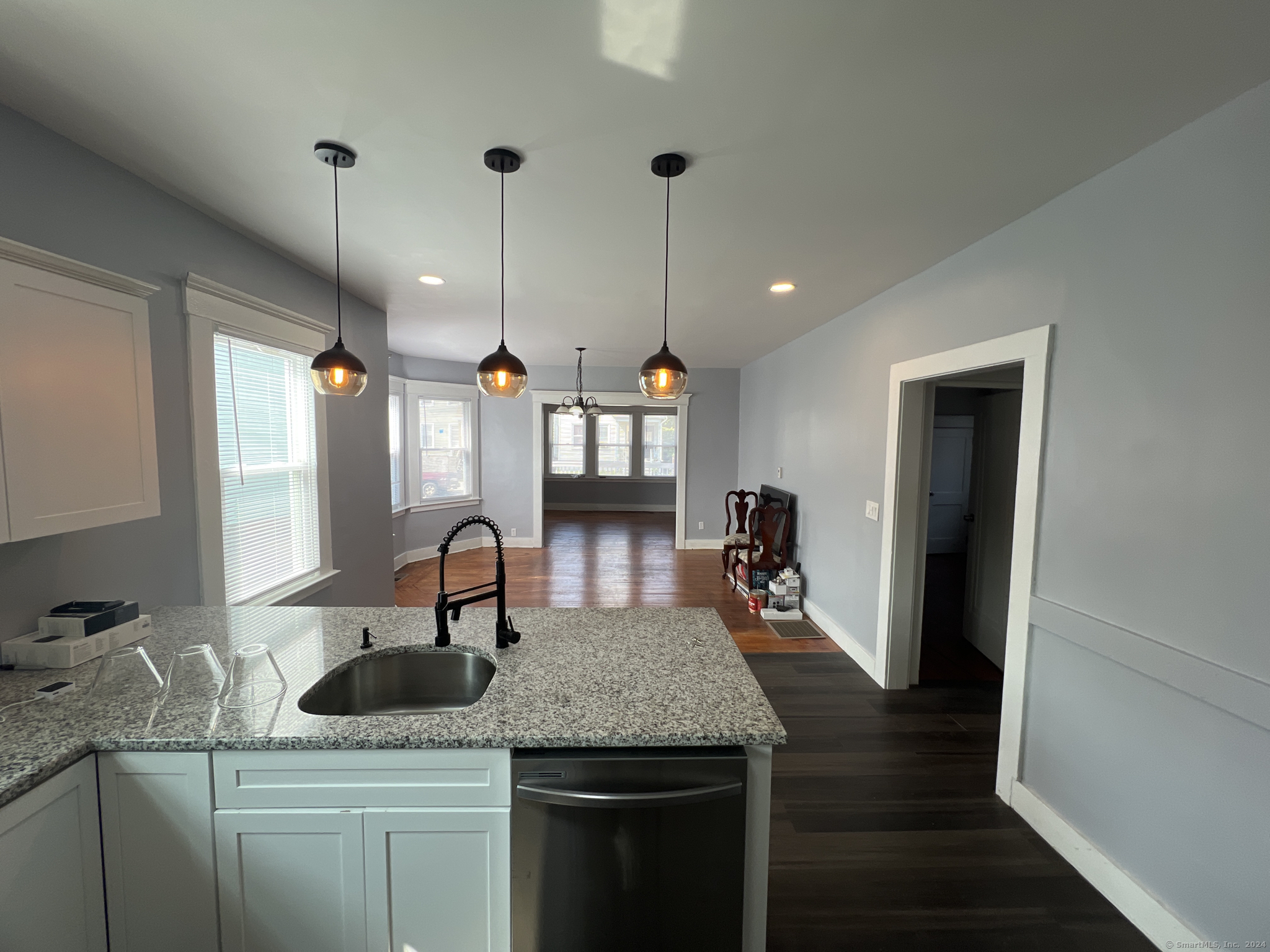 Kitchen with granite island and pendant lights opening onto a hardwood-floored dining area.