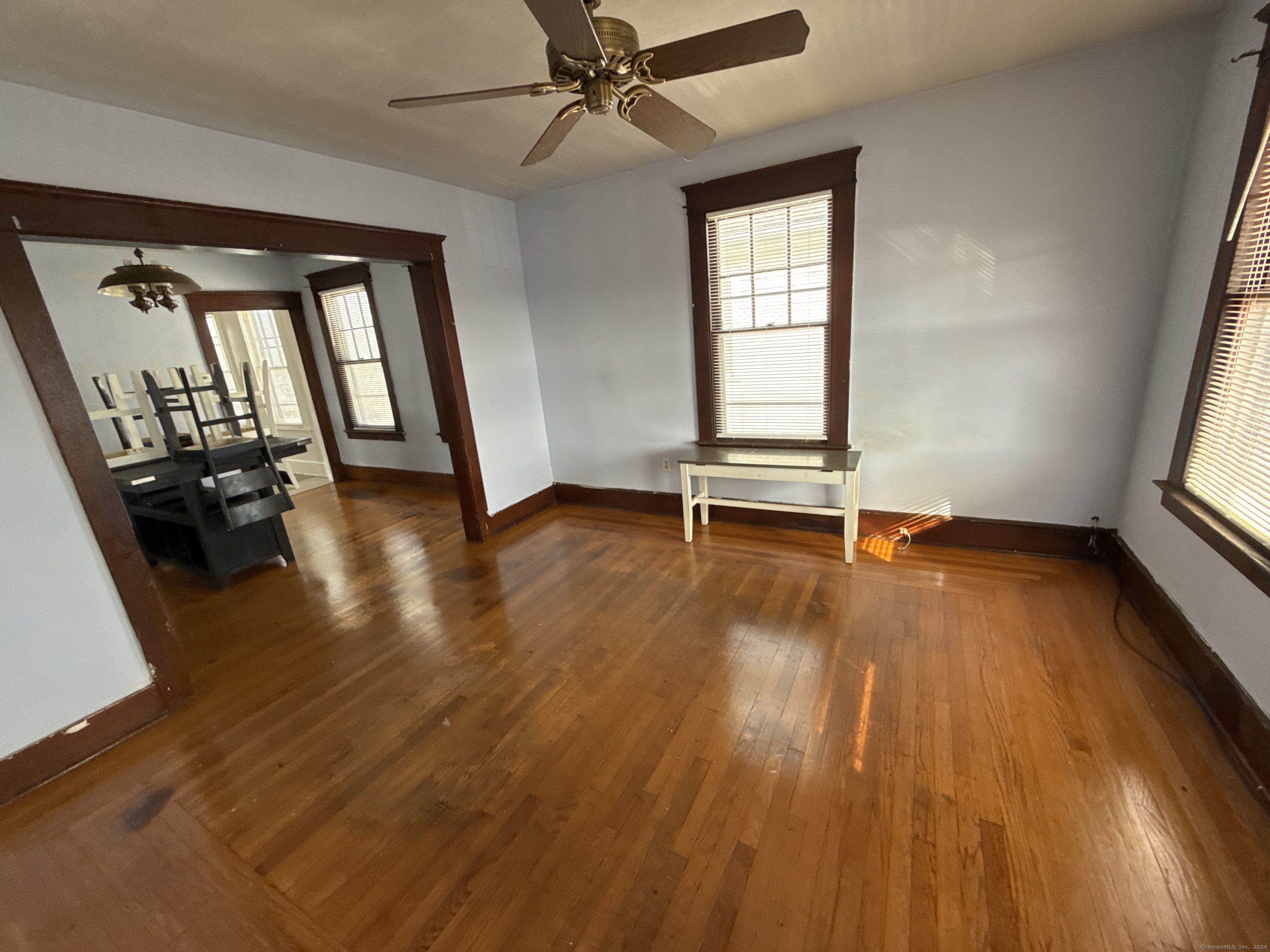 Living room with polished hardwood floors, dark wood trim, and a wide opening to the dining area.