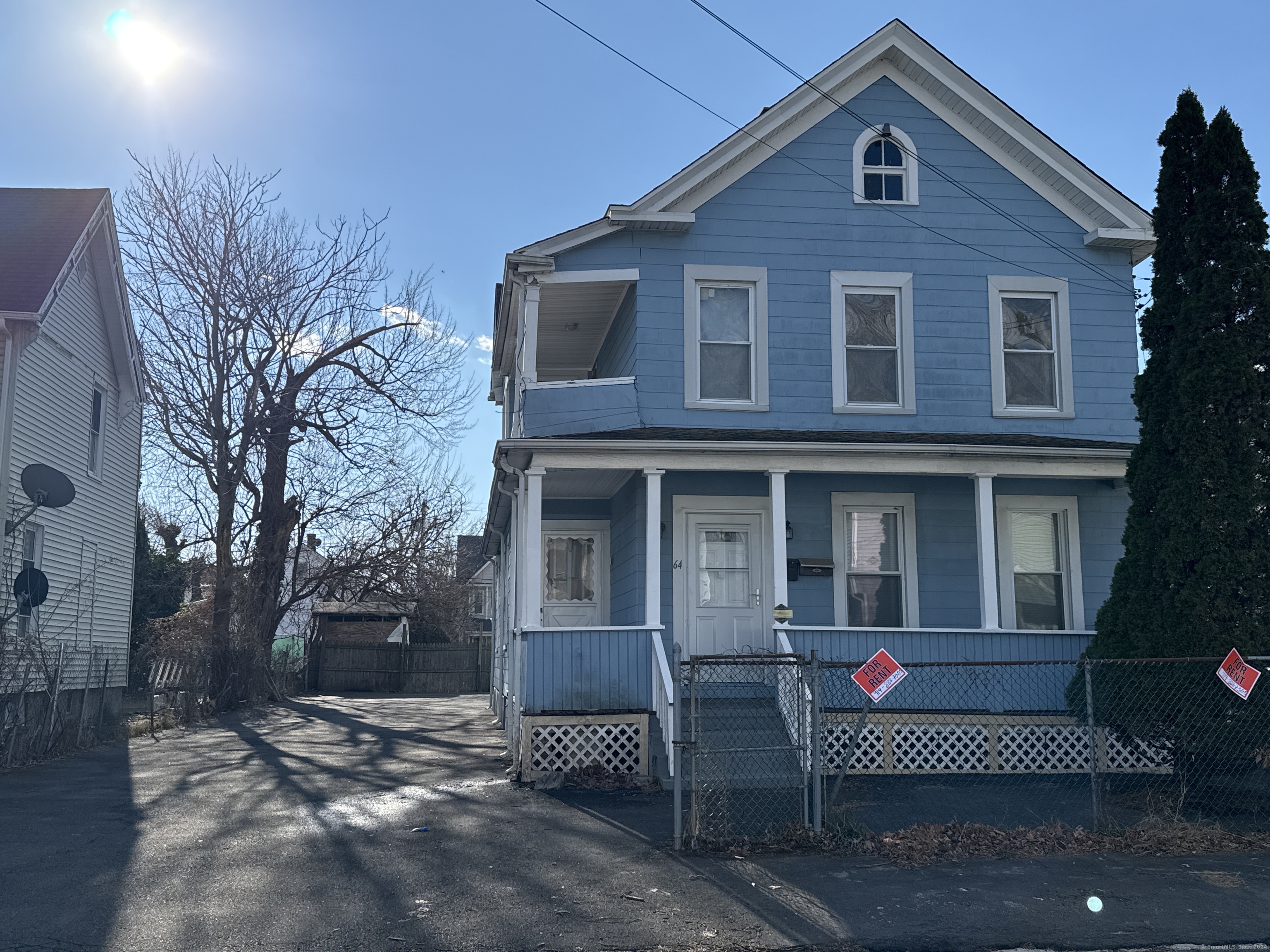Blue two-story house with a covered porch, chain-link fence, and two For Rent signs.