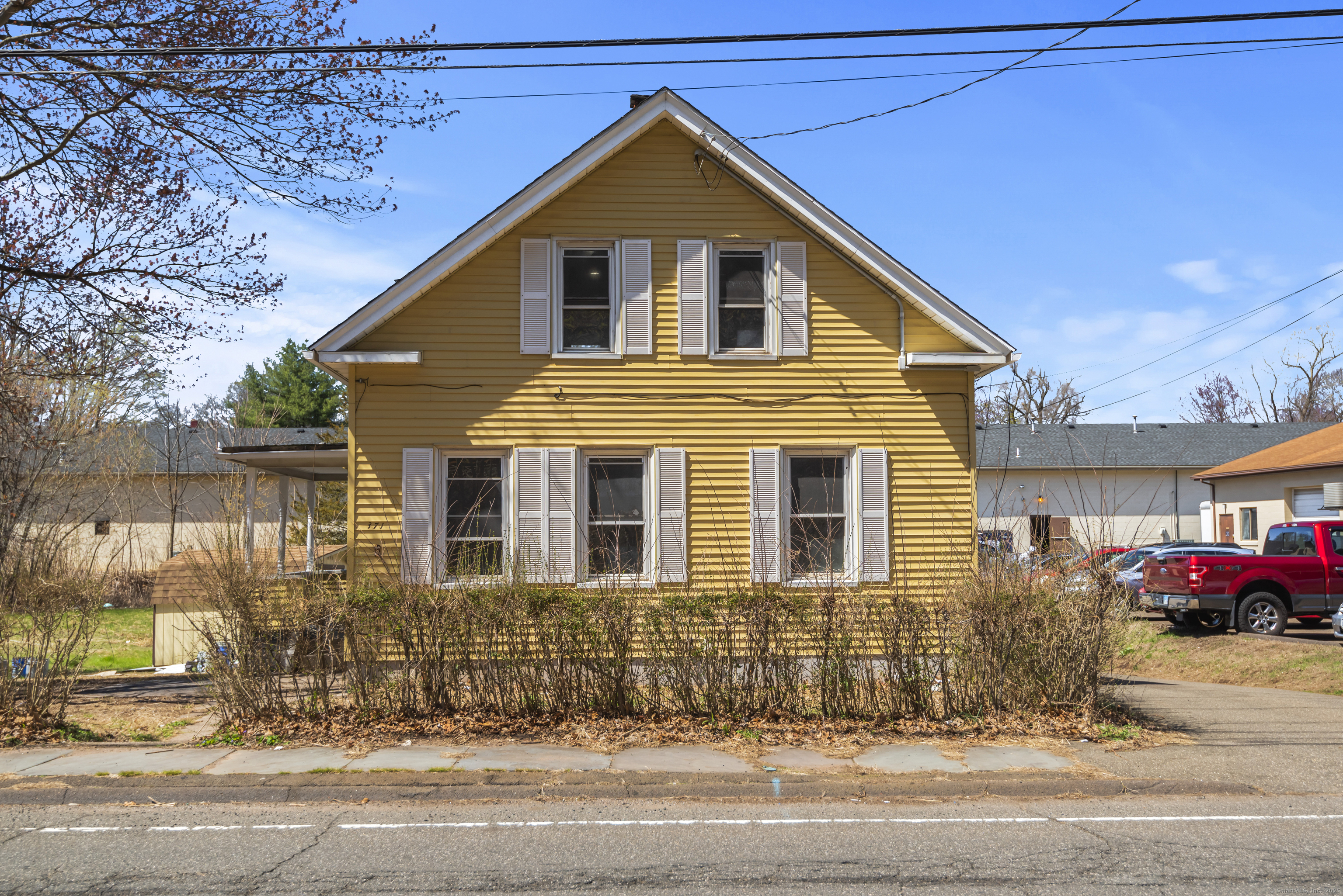 Yellow two-story house with white shutters, photographed from across the street.