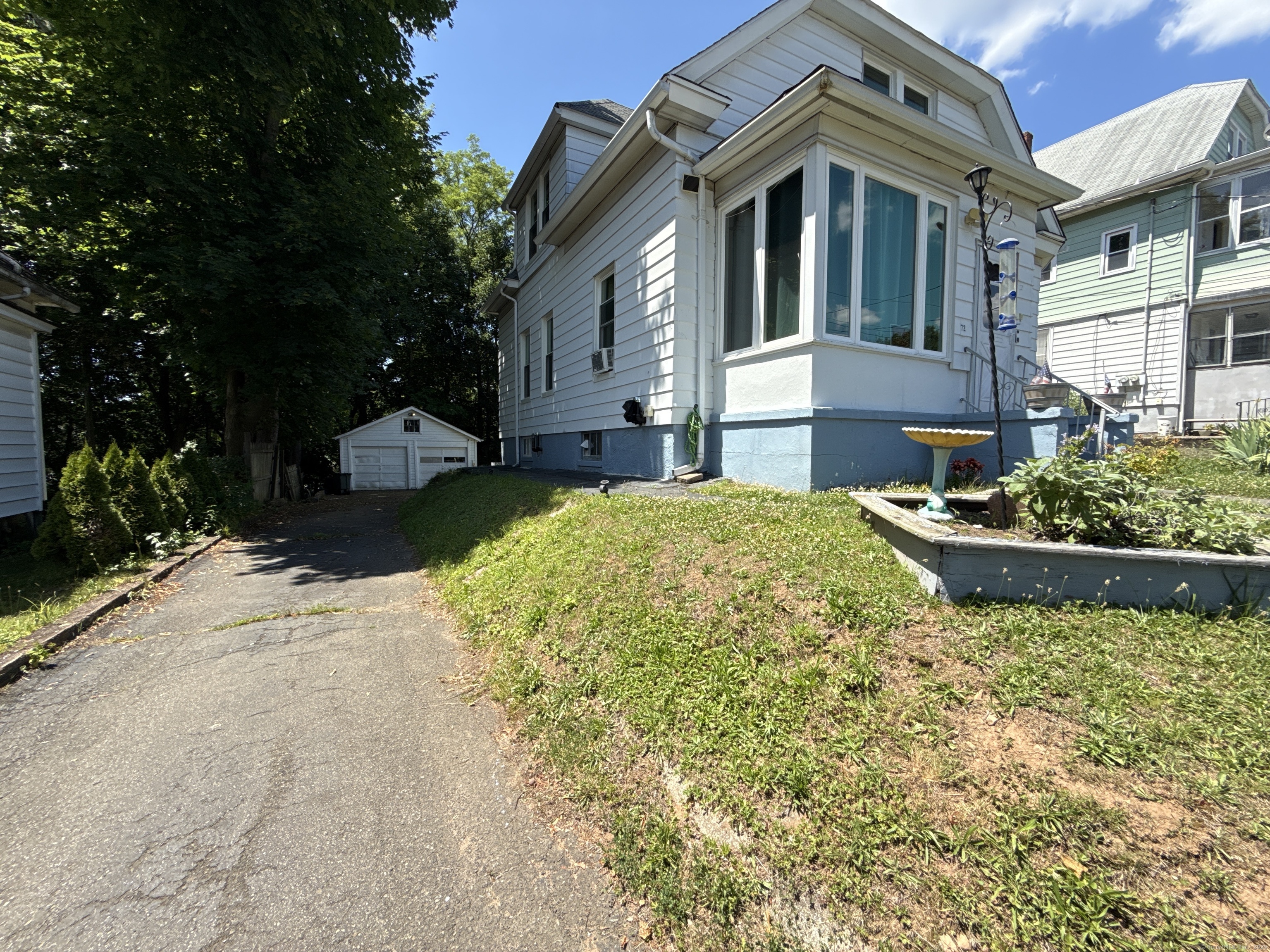 White two-story house with an enclosed front porch, driveway, detached garage, and raised garden bed.