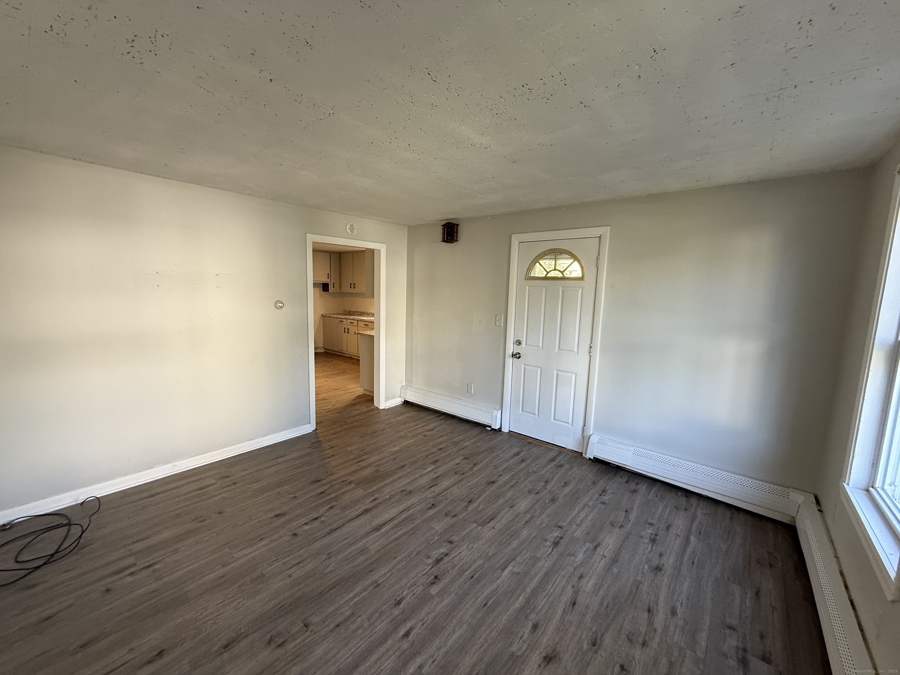 Empty living room with plank flooring, a half-round-window entry door, and a kitchen doorway.
