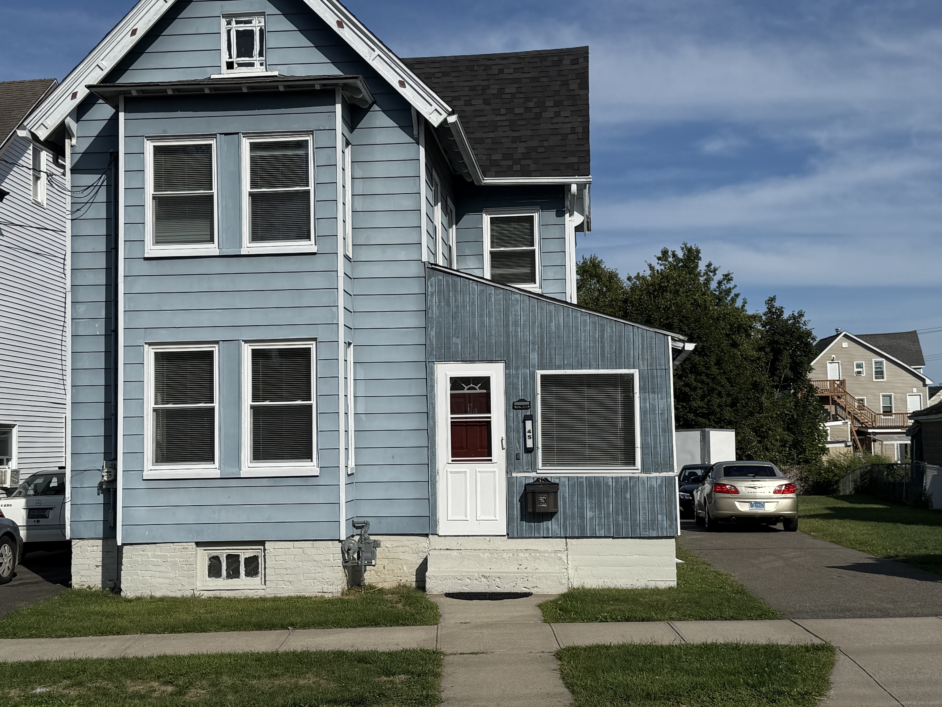 Blue-gray gabled house with white trim, red front door, and cars parked beside it.