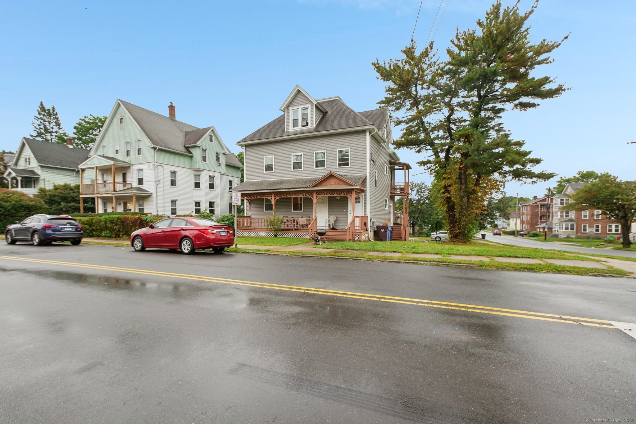 Gray multi-story house with a decorative covered porch beside a tree-lined street.
