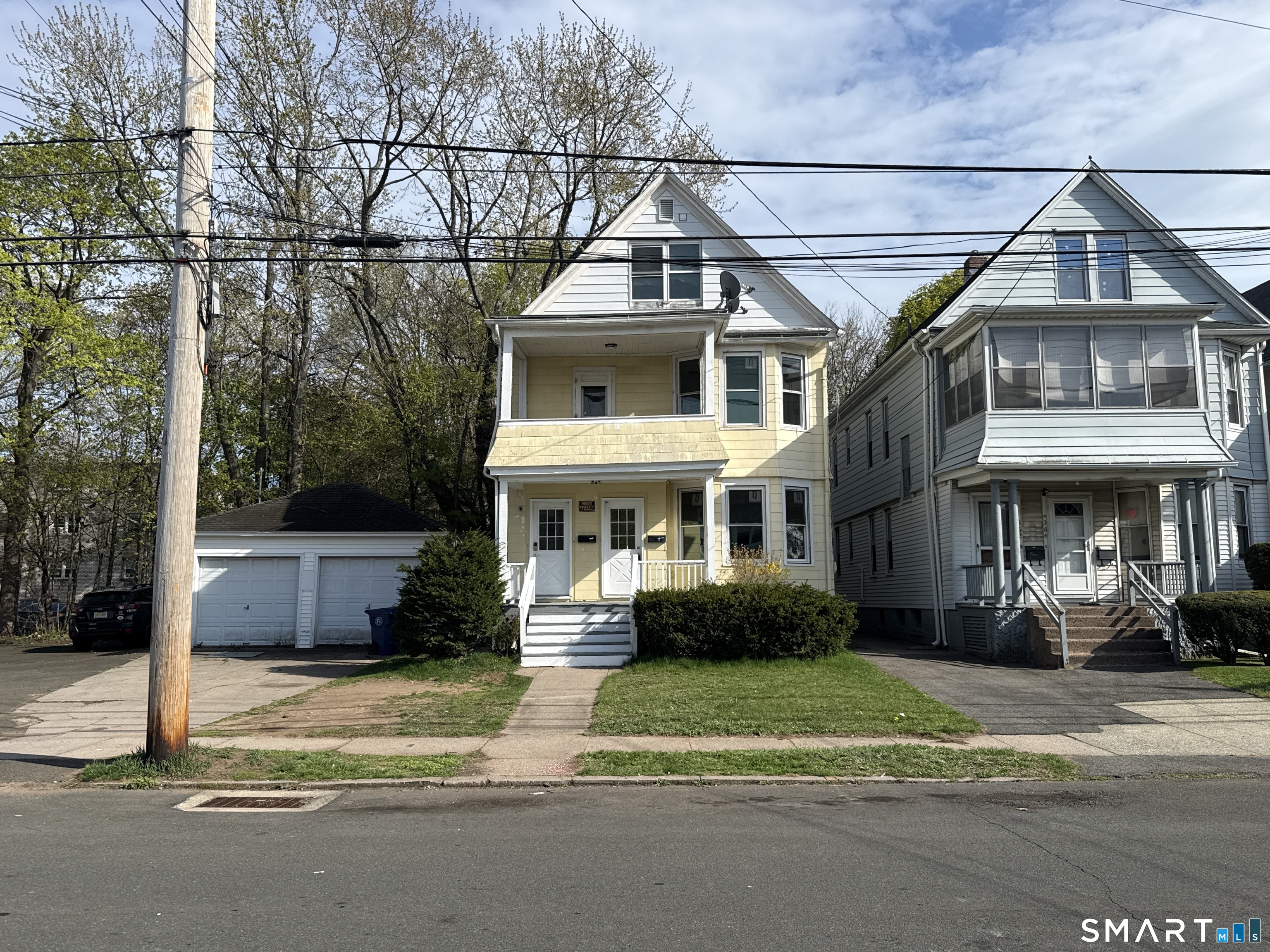 Yellow gable-roofed house with a covered front porch and detached garage, between neighboring homes.