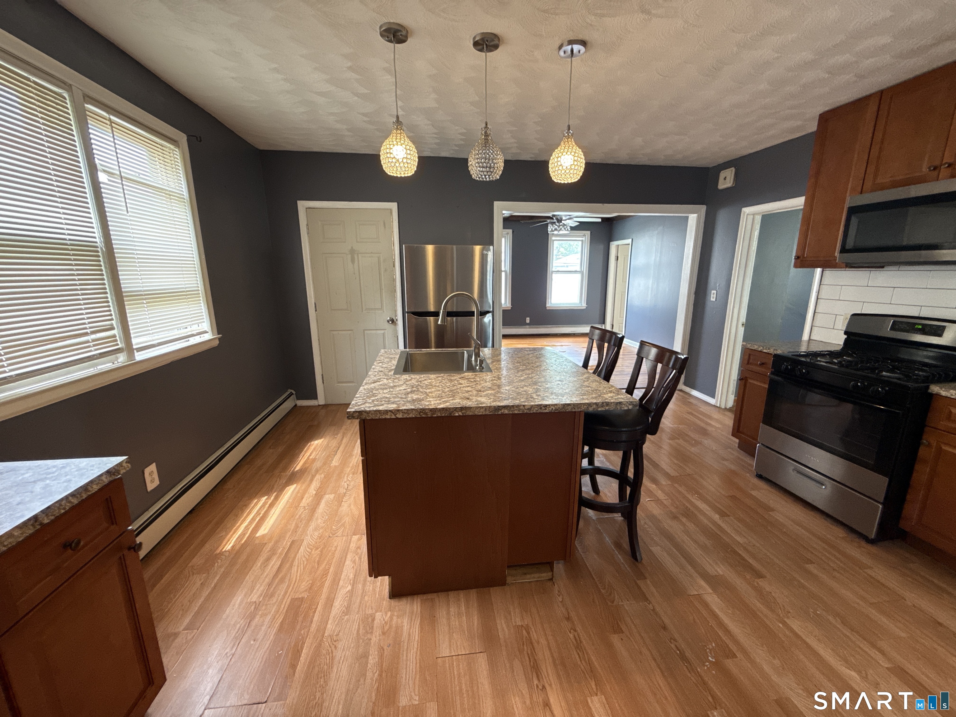 Kitchen with a granite-topped island, pendant lights, and stainless steel appliances.