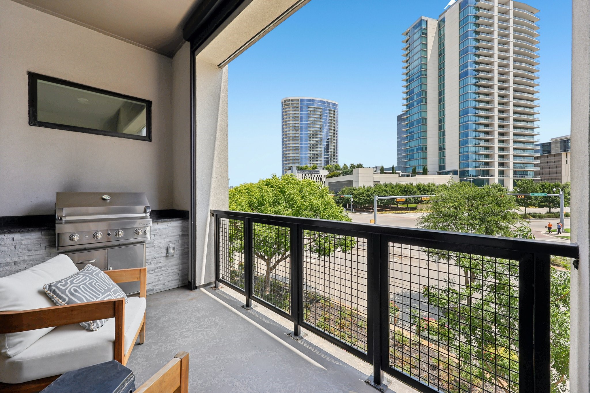 Apartment balcony with built-in grill, seating, and views of downtown towers.