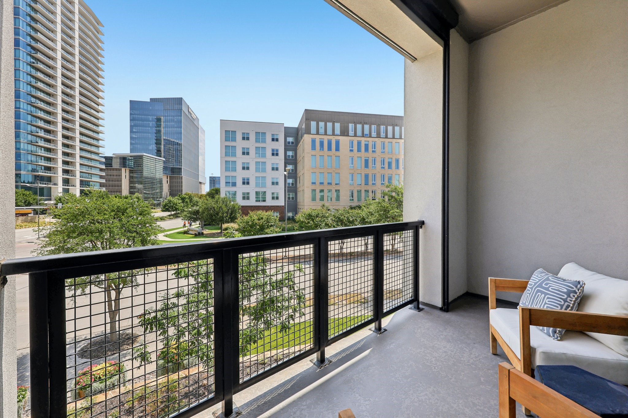 Furnished apartment balcony overlooking leafy streets and modern city buildings.