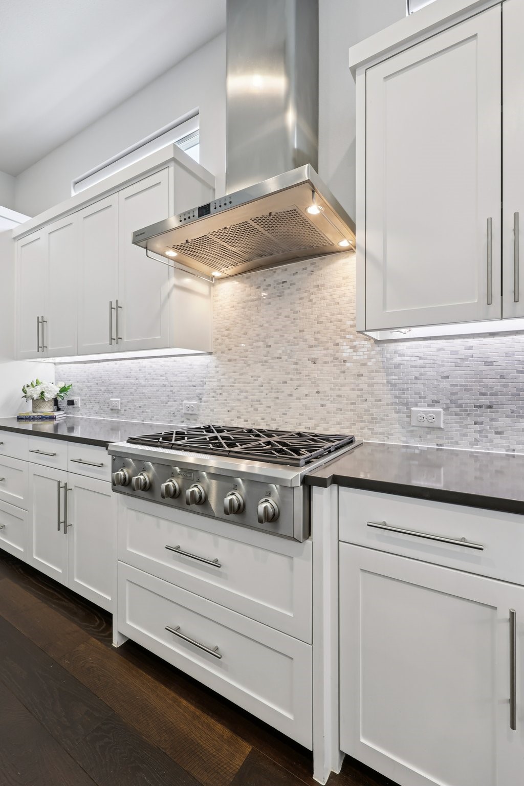 Modern kitchen with white cabinets, stainless steel range, and light mosaic backsplash.