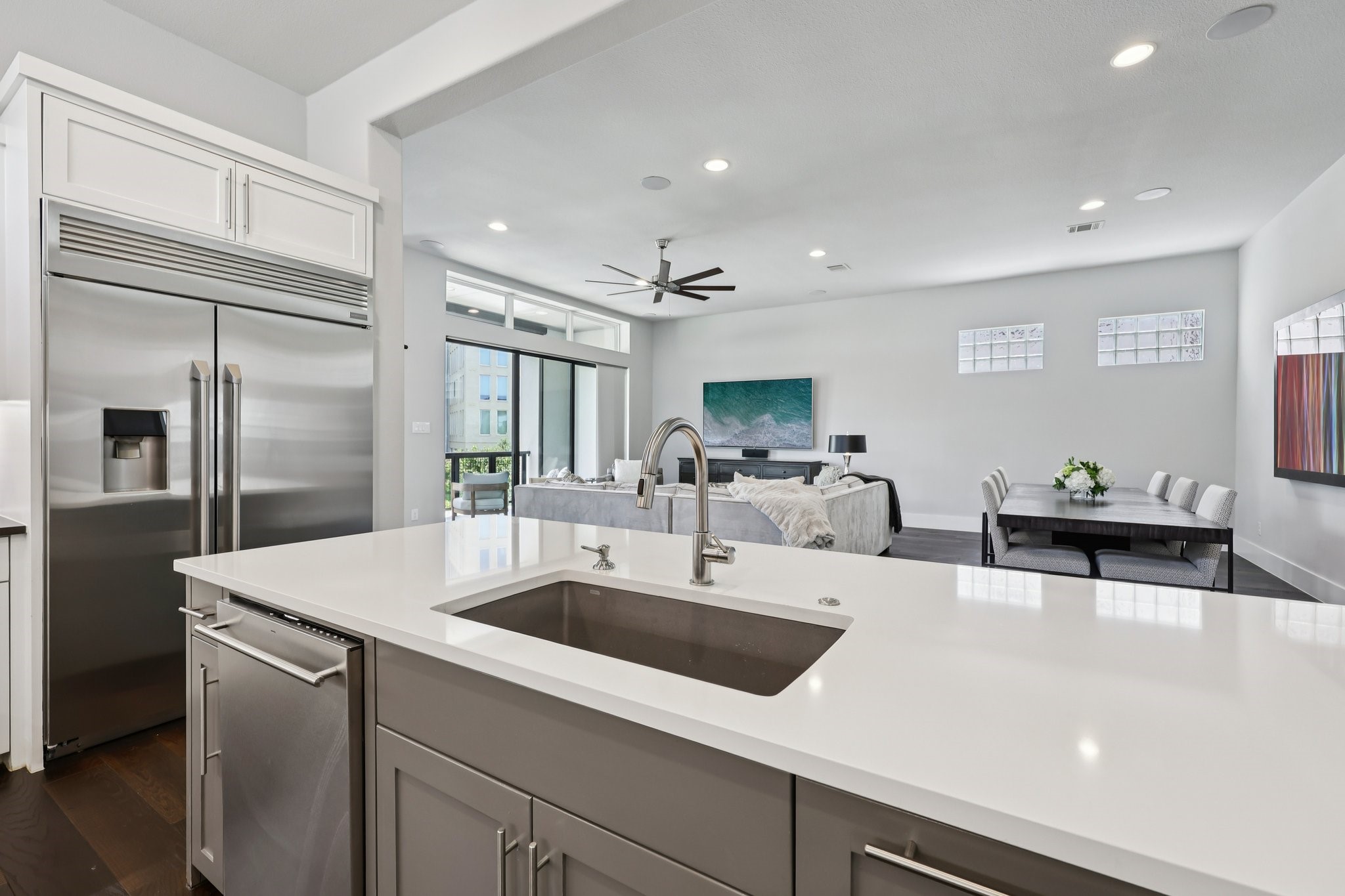 Modern kitchen with a white island and stainless appliances overlooking furnished living and dining areas.