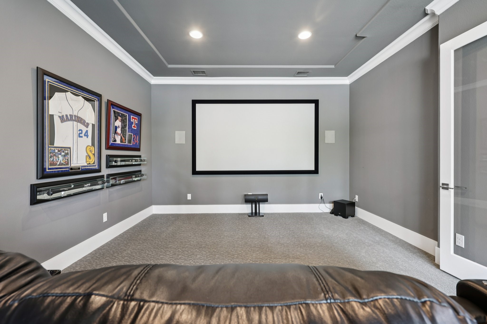 Media room with a large projection screen, framed baseball memorabilia, and leather seating.