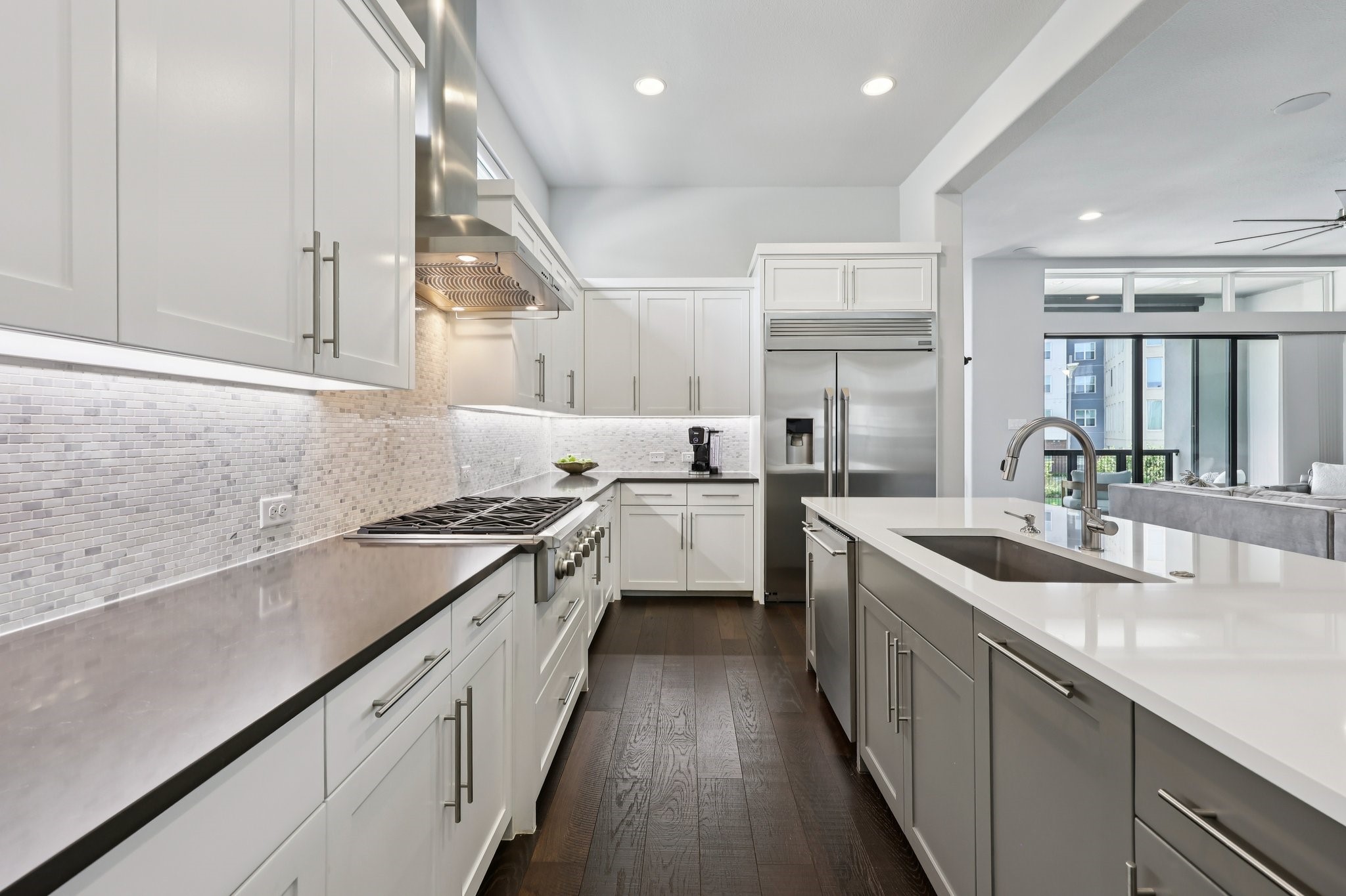 Modern white kitchen with a large island, stainless-steel appliances, and dark wood floors.