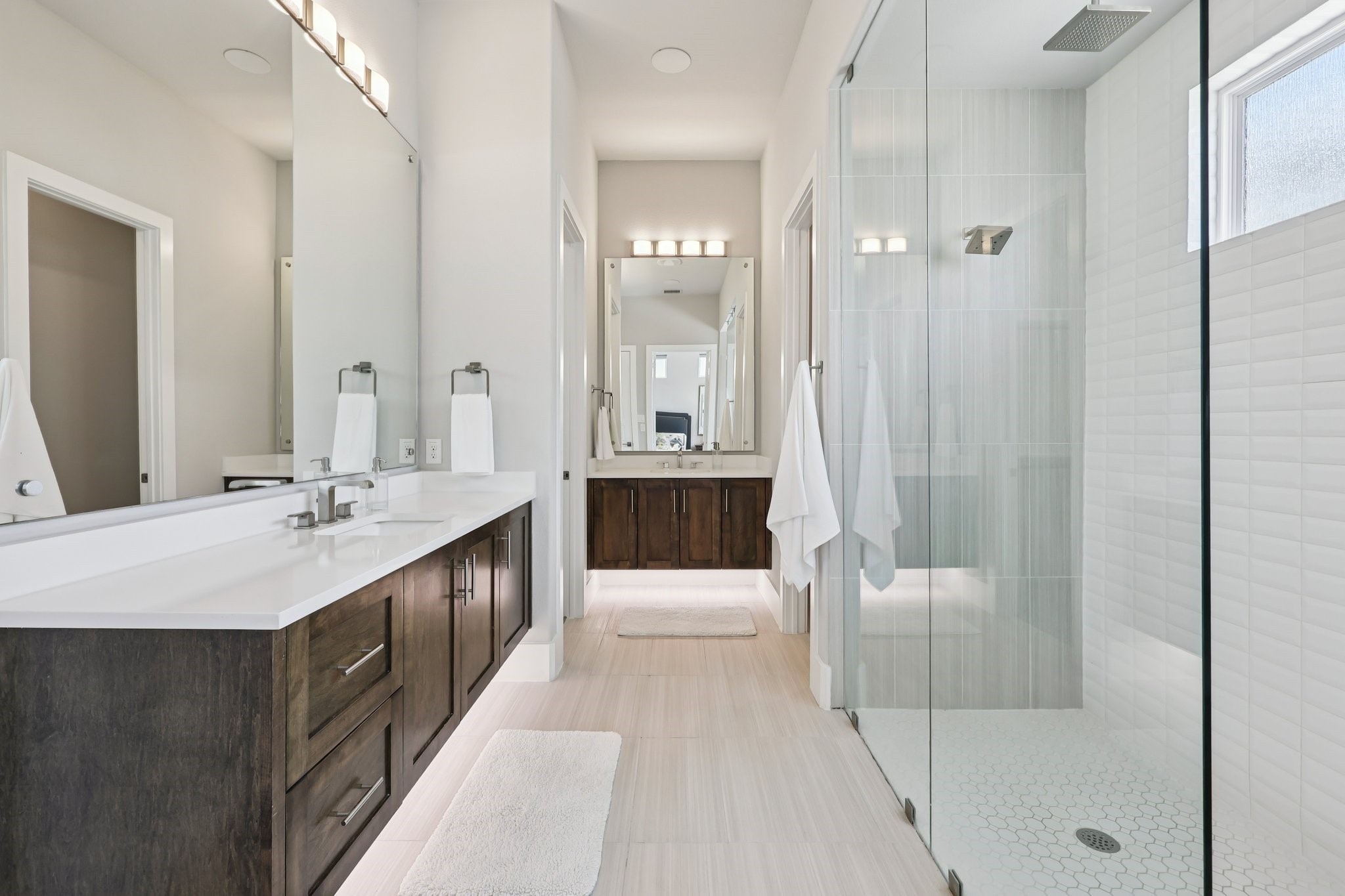 Modern bathroom with dark wood double vanity and glass walk-in shower with white tile.