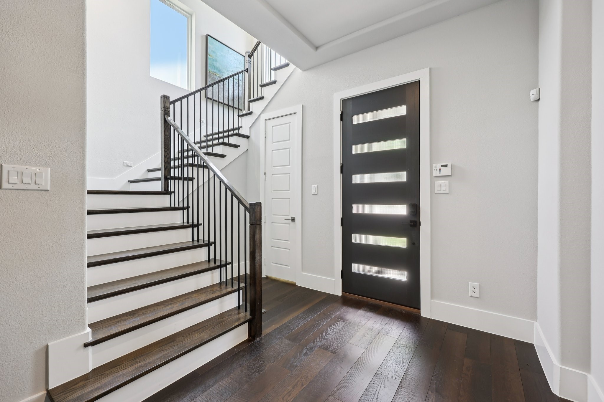 Entry foyer with dark wood staircase, black metal railing, and modern front door.