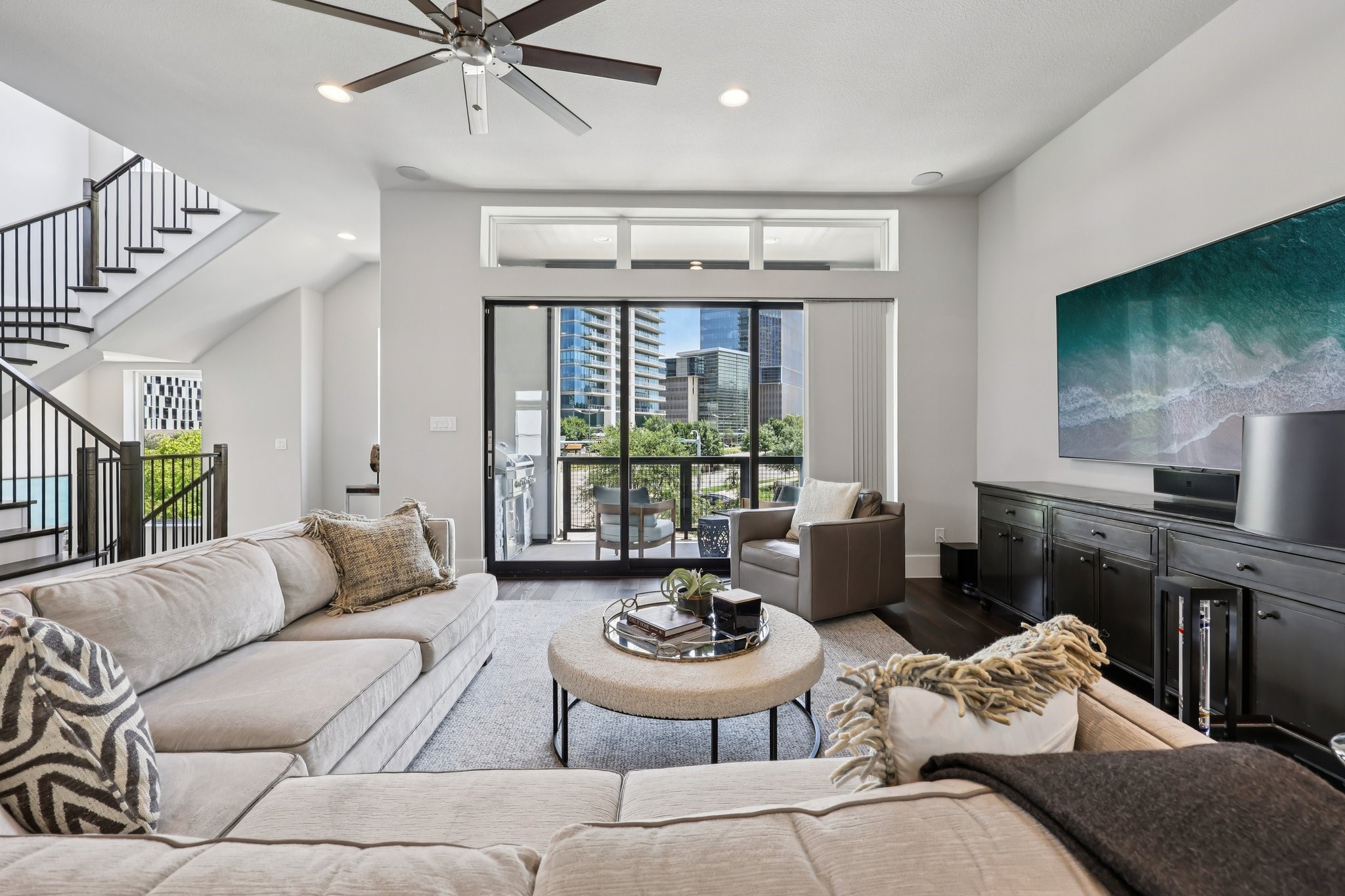 Living room with a staircase, sliding balcony doors, and city buildings visible outside.