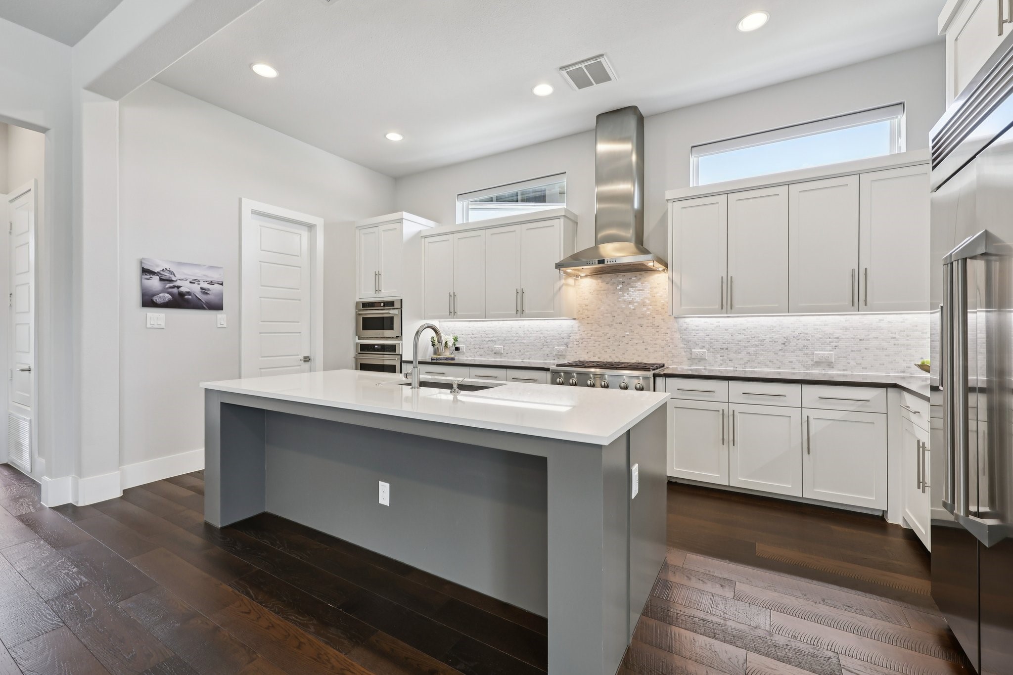 Modern kitchen with white cabinets, a large gray island, stainless steel appliances, and dark wood floors.