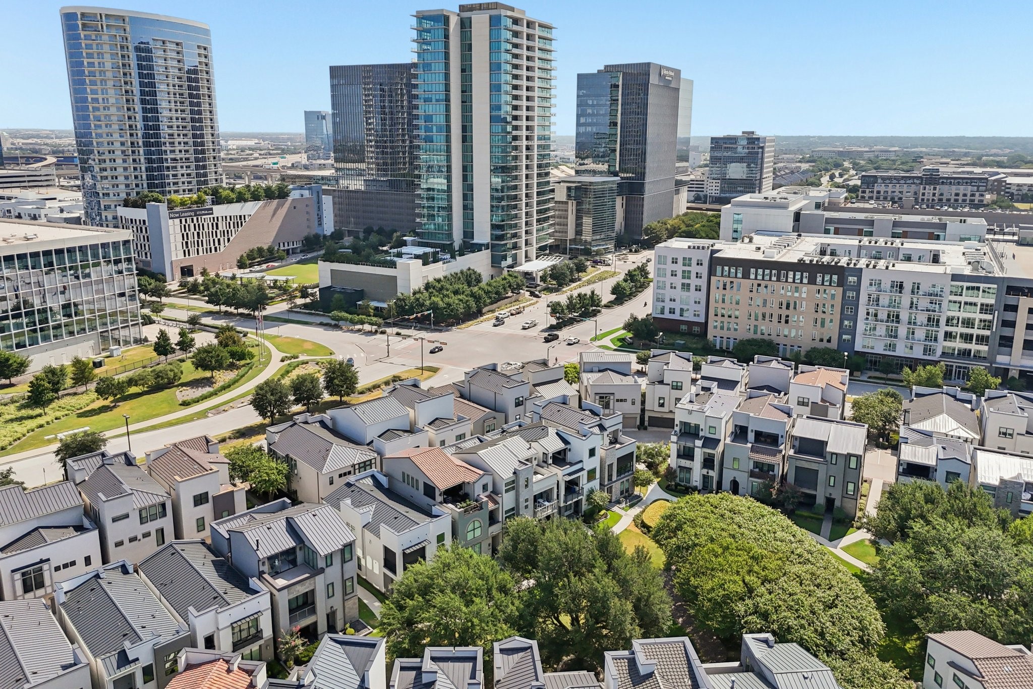Aerial view of modern townhouses and landscaped grounds, with a high-rise city skyline beyond.