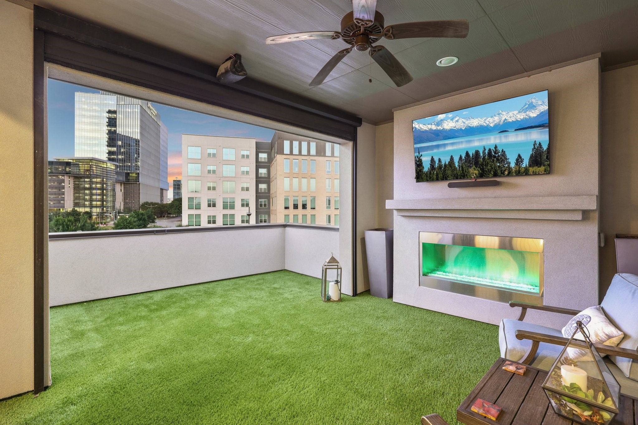 Covered balcony with artificial turf, fireplace, and city views.