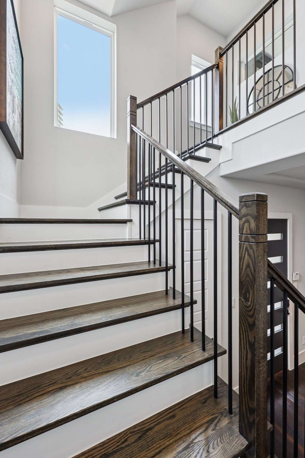 Multi-level staircase with dark wood treads, black metal railings, and a tall window.