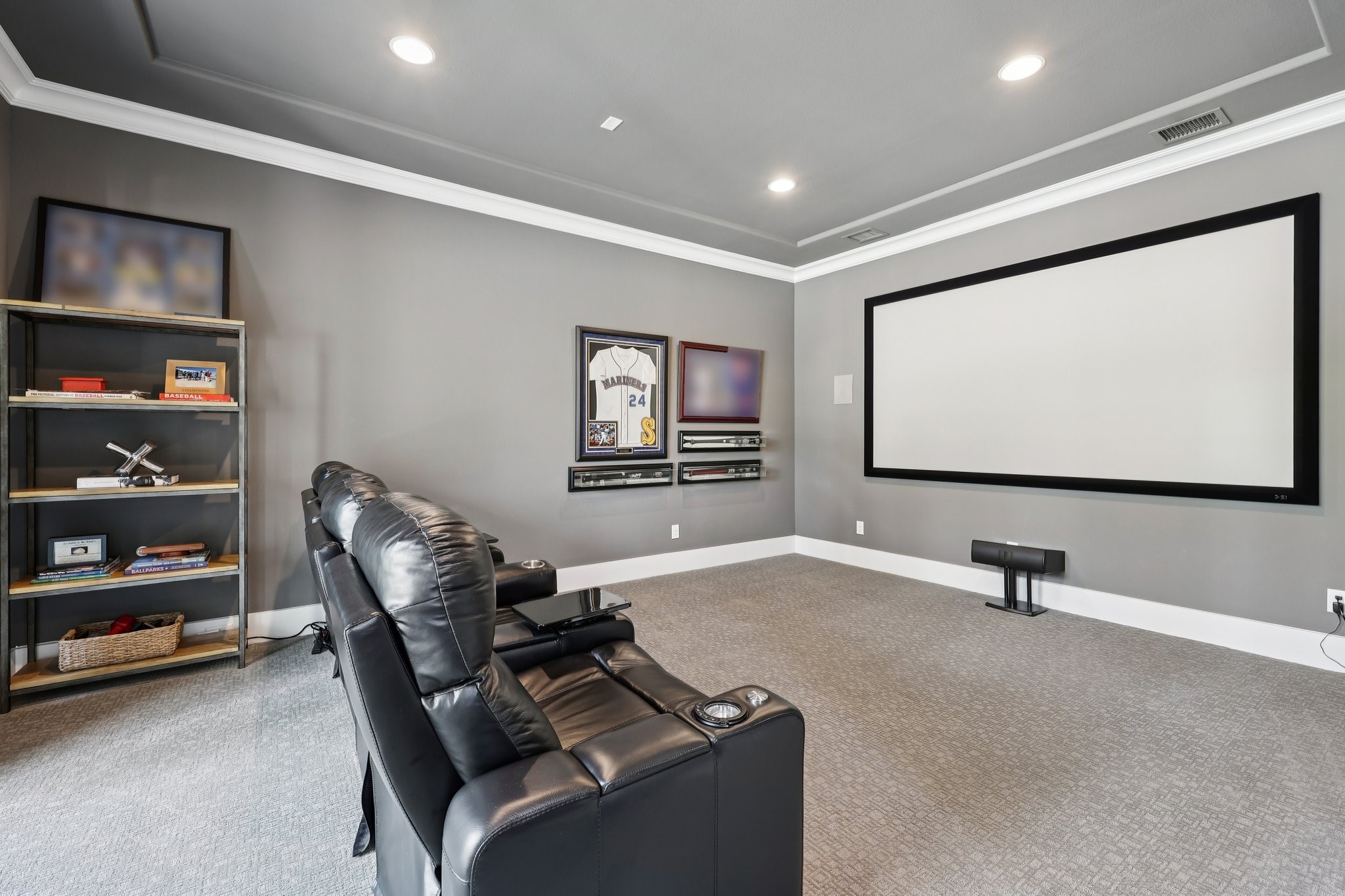 Home theater with a large projection screen, black leather recliners, and baseball memorabilia.
