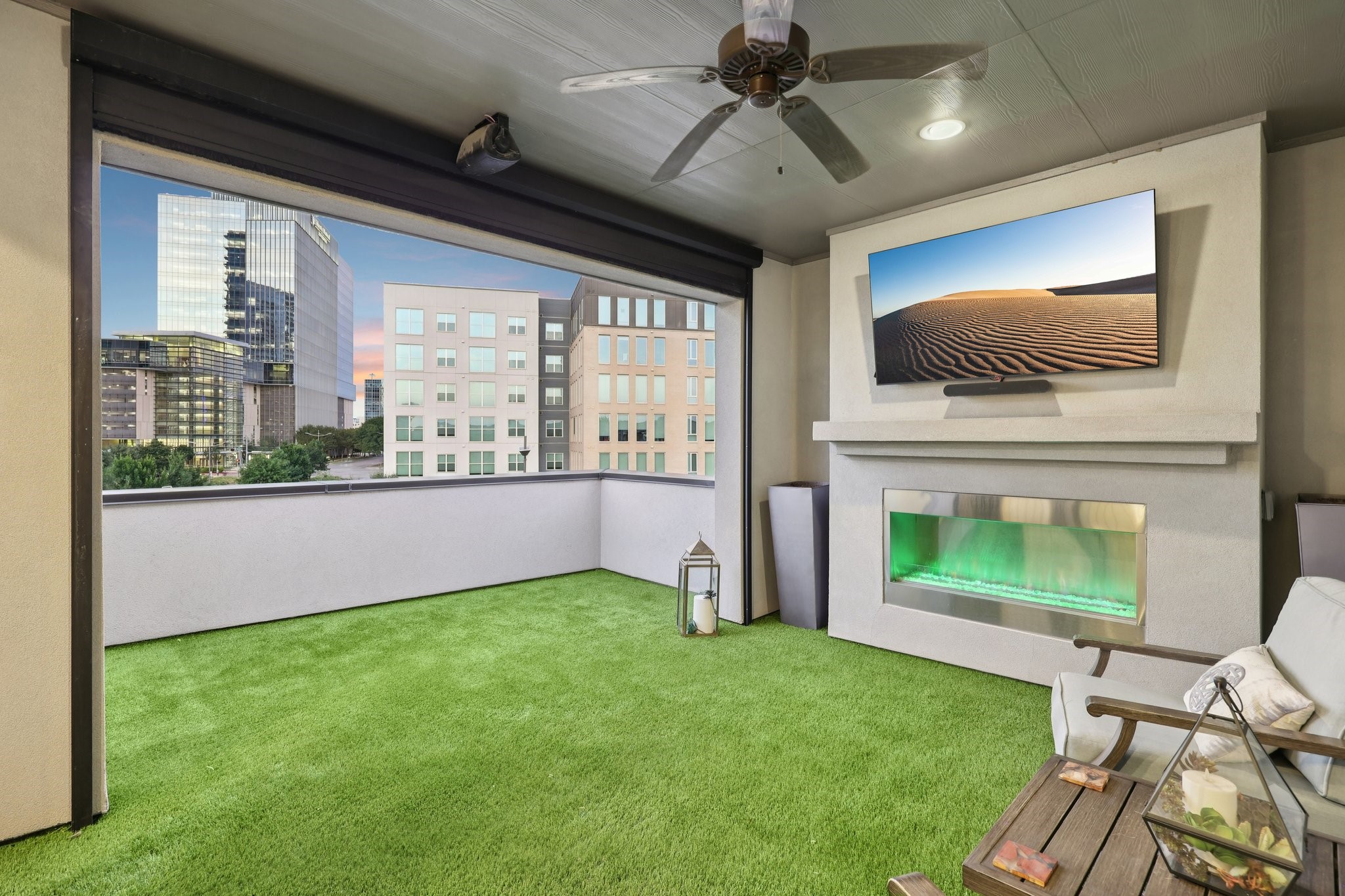 Covered rooftop patio with artificial turf, a built-in fireplace, and views of city buildings.