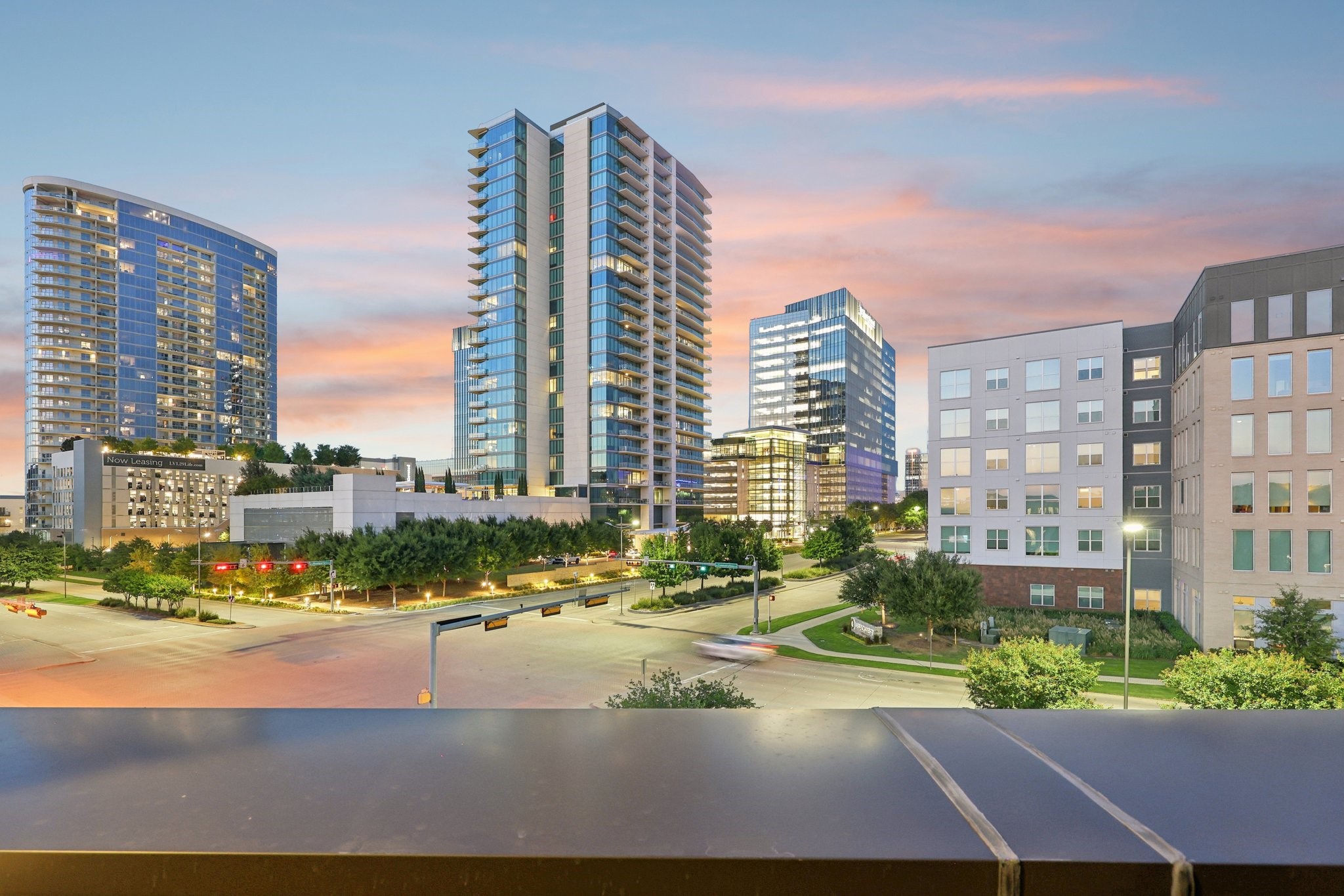 Modern residential towers and mid-rise buildings surround a landscaped intersection at dusk.