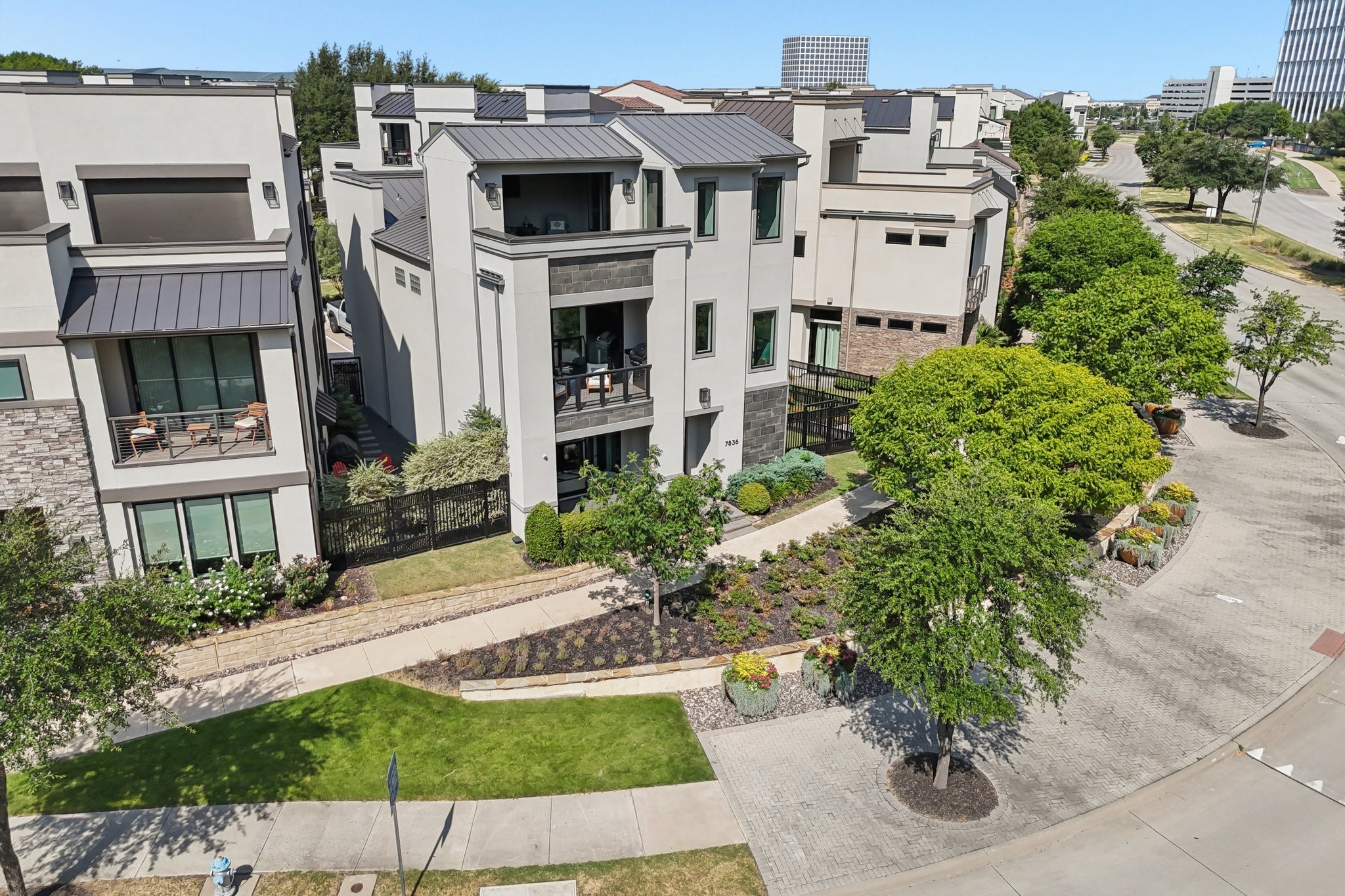 Modern three-story townhouse with two balconies, landscaped gardens, and a paved corner street.