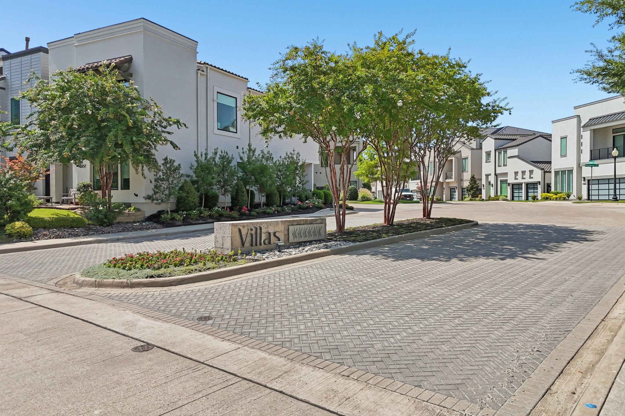Modern white townhomes line a landscaped street beside a stone Villas entrance sign.