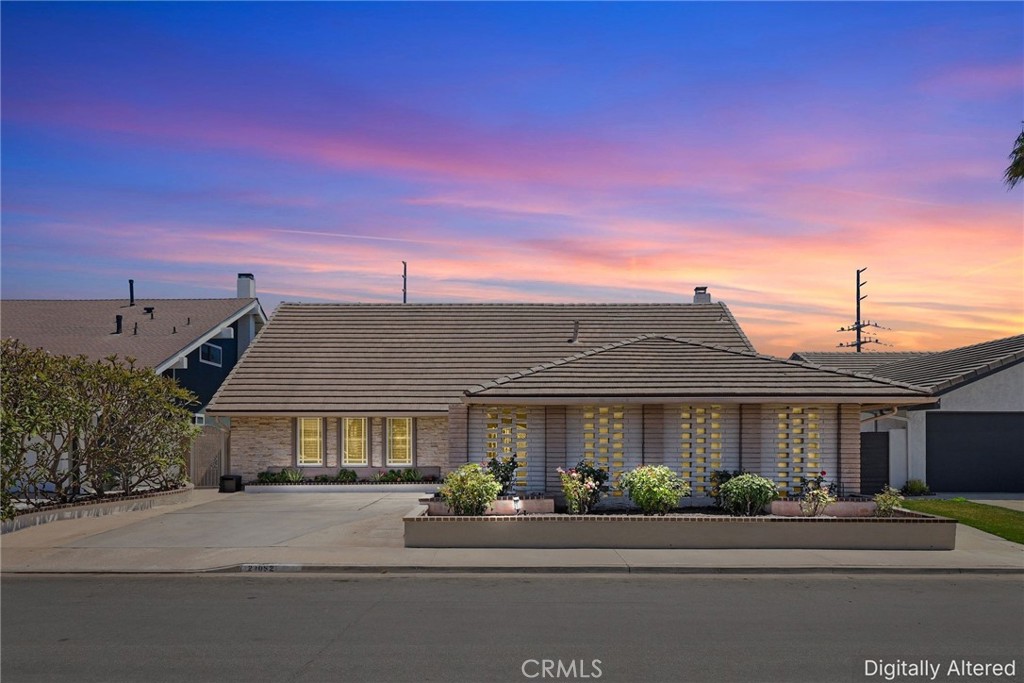 Single-story brick home with a tiled roof and front garden beneath a pink dusk sky.