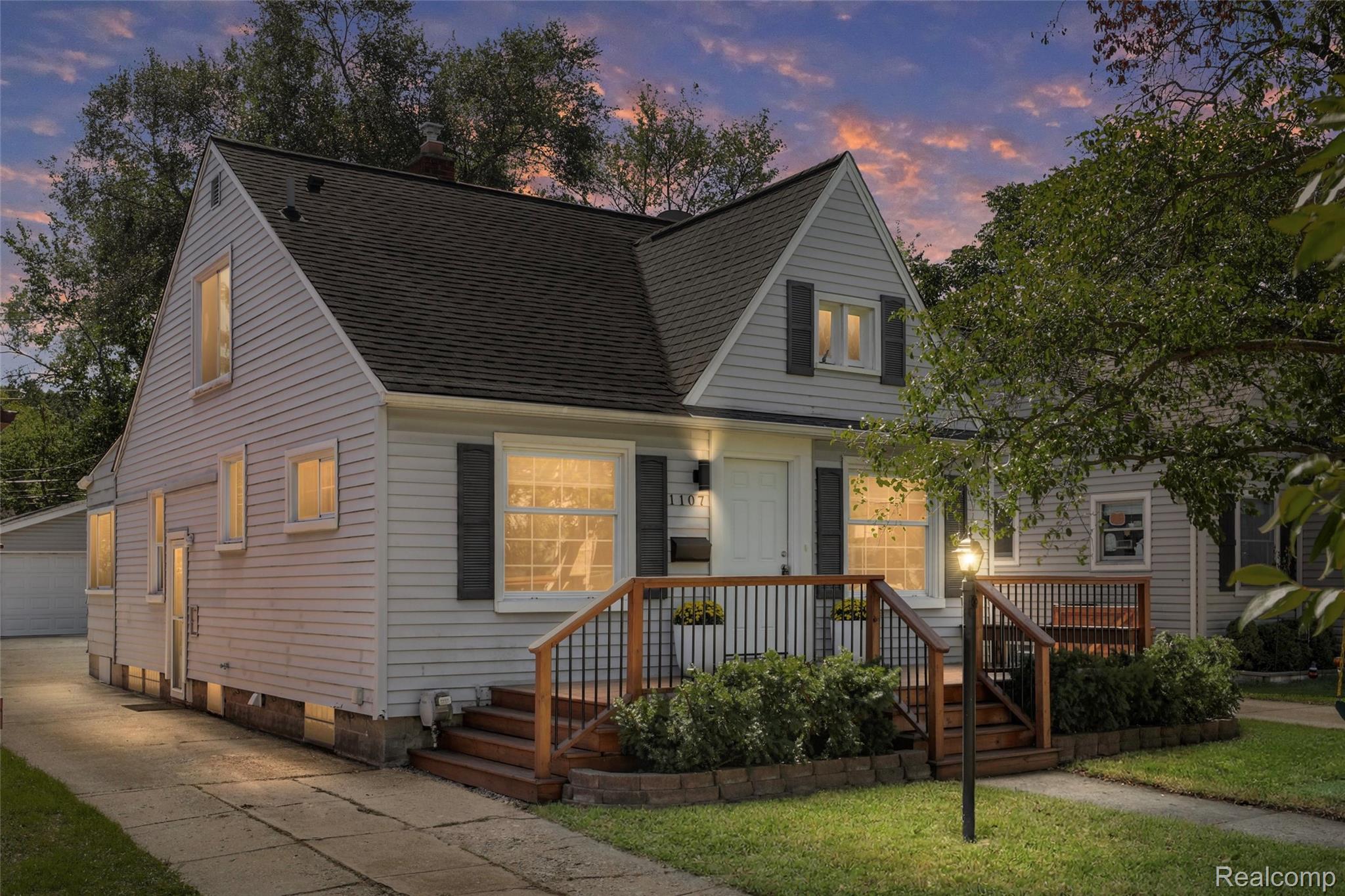 Two-story light-sided house with a raised wooden porch and warmly lit windows at dusk.