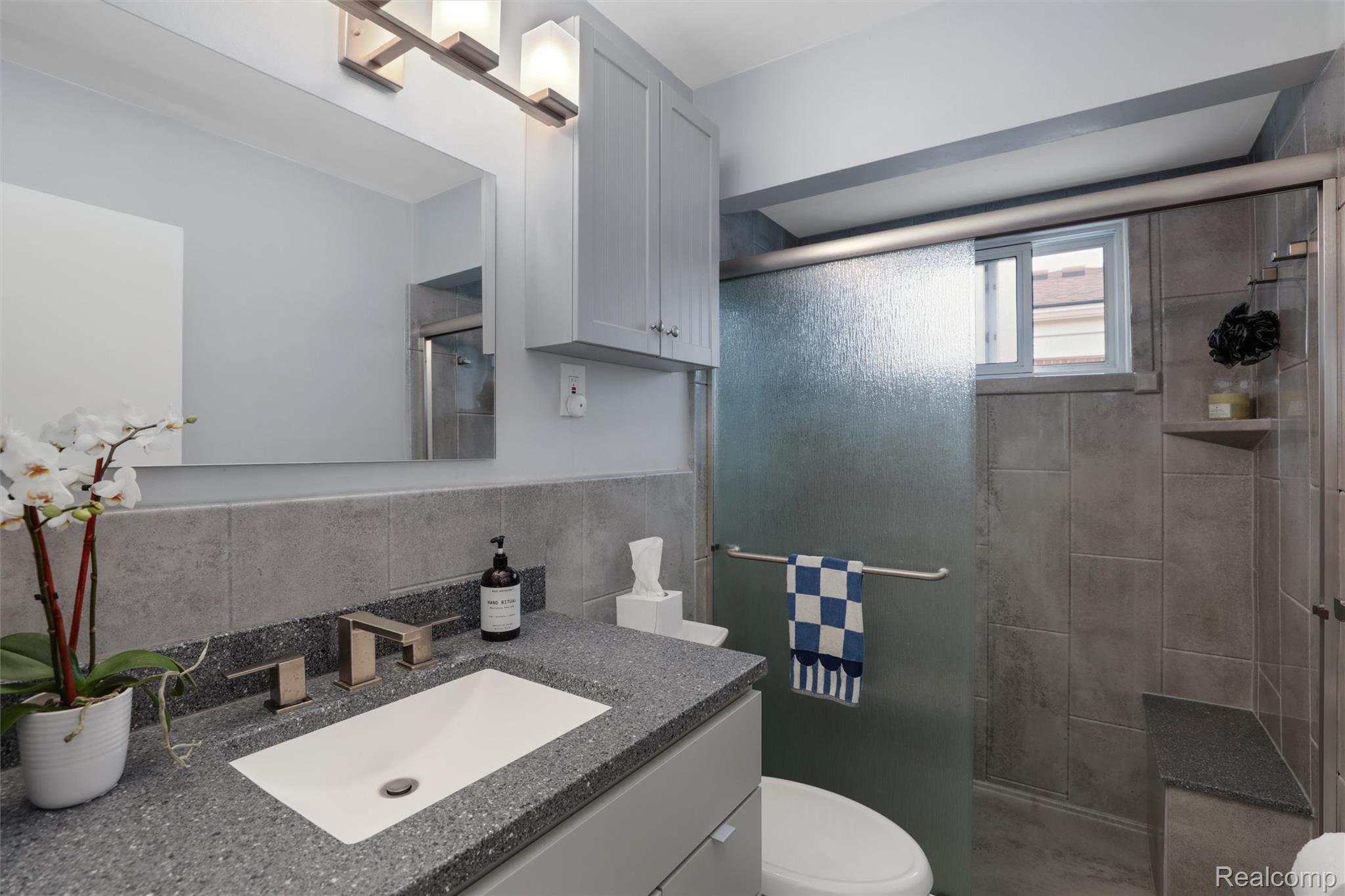 Bathroom with gray tile, stone vanity, and frosted-glass shower.