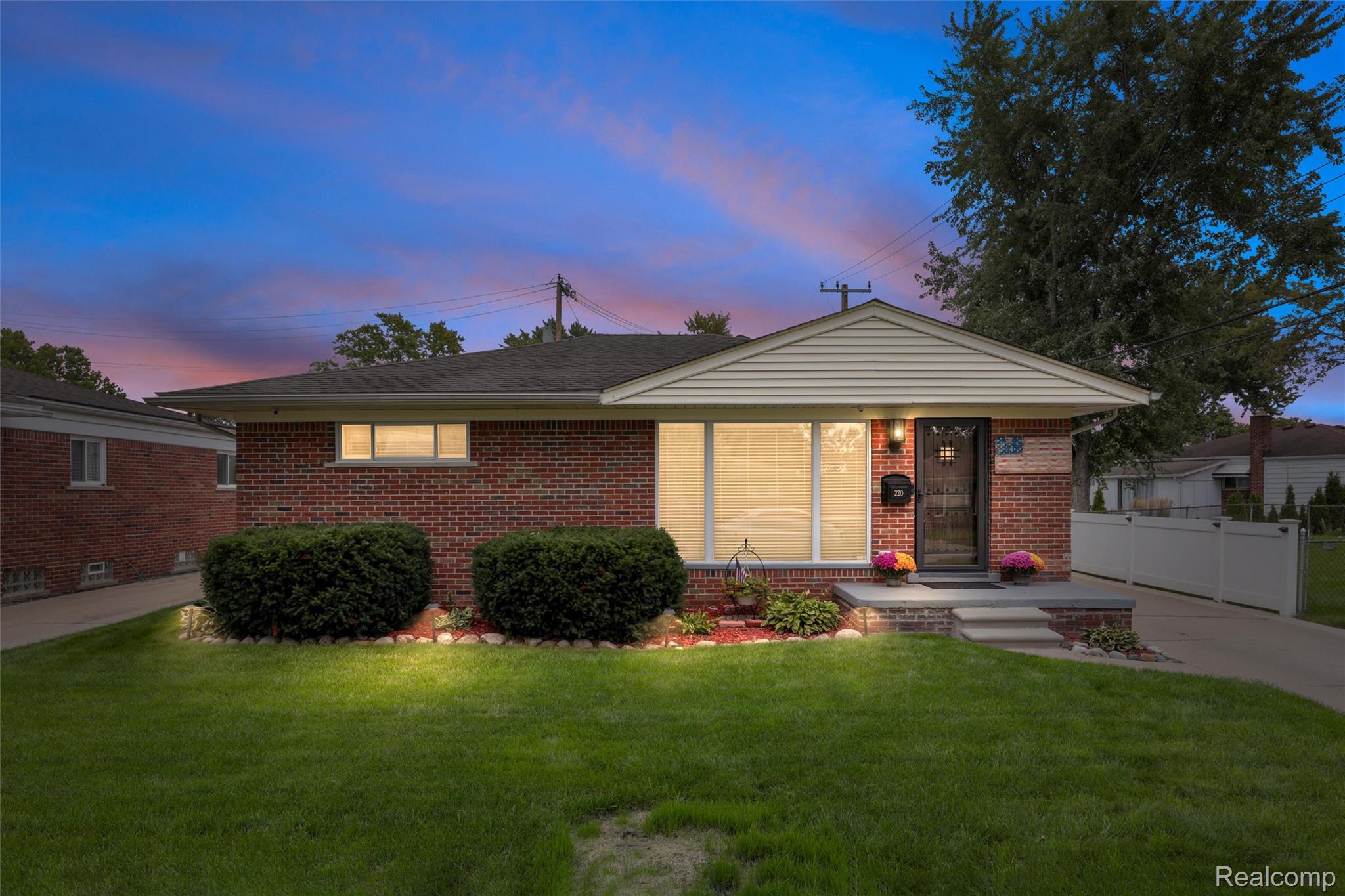 Single-story brick house with a white gabled entry, landscaped lawn, and illuminated windows at dusk.