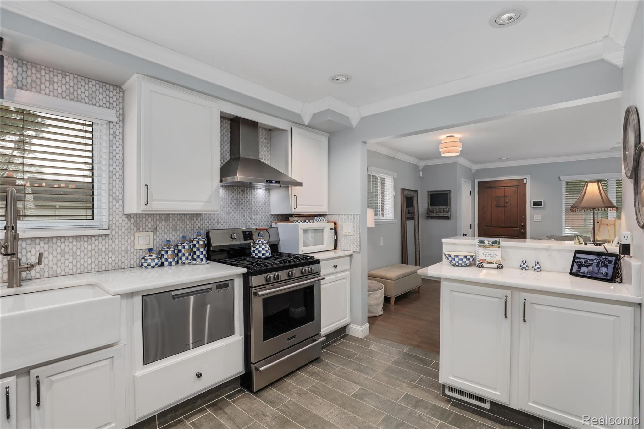 Renovated kitchen with white cabinets, patterned tile backsplash, stainless appliances, and a peninsula opening to the entryway.