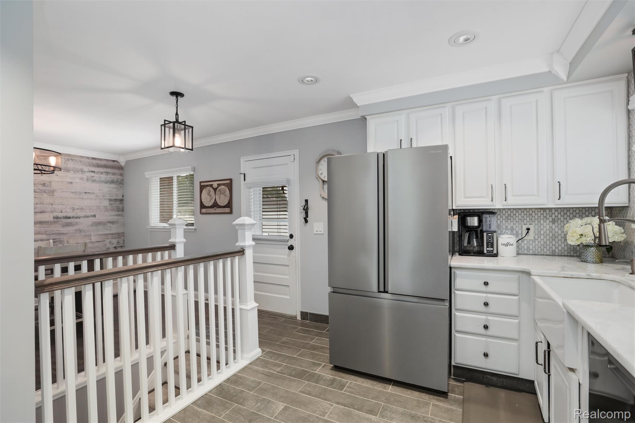 Kitchen with white cabinets, stainless steel refrigerator, patterned backsplash, and an adjoining stair railing.