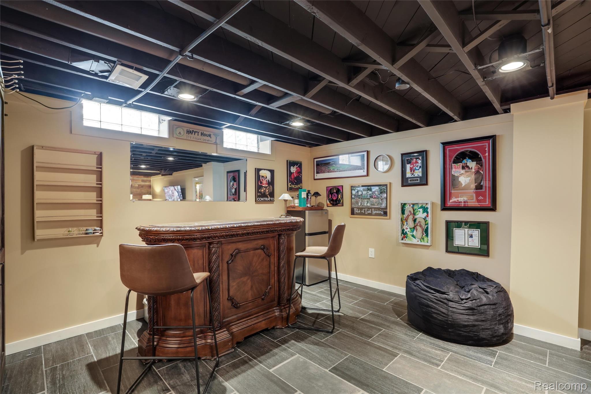 Basement bar with an ornate wood counter, framed wall art, and a black beanbag chair.