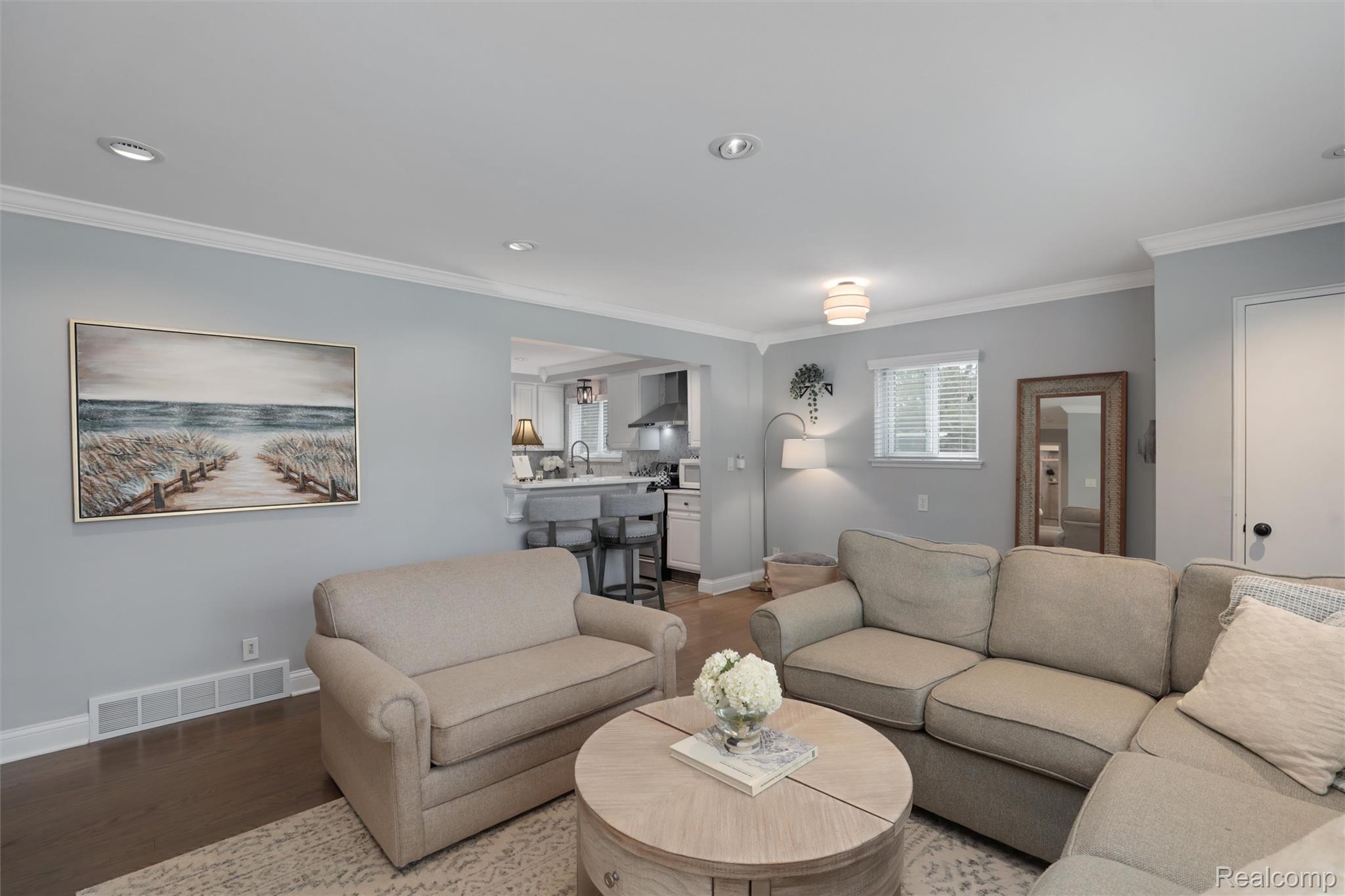 Living room with beige sofas, a round coffee table, and an open kitchen beyond.