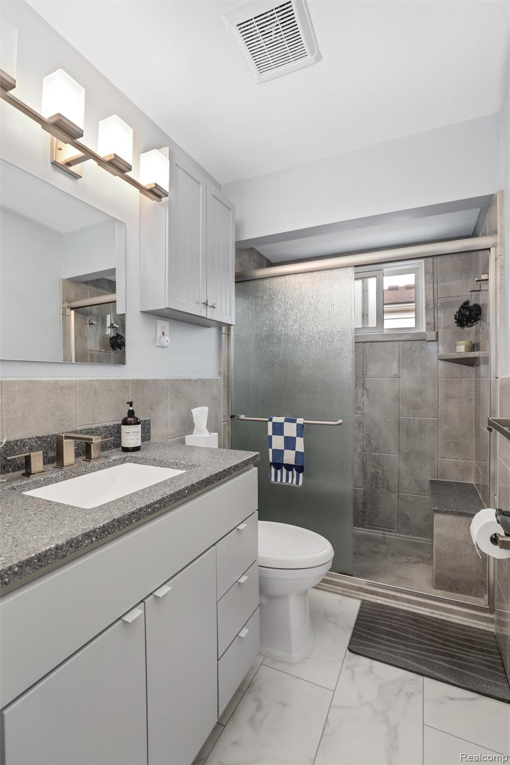 Bathroom with a gray vanity and tiled walk-in shower behind a frosted-glass door.
