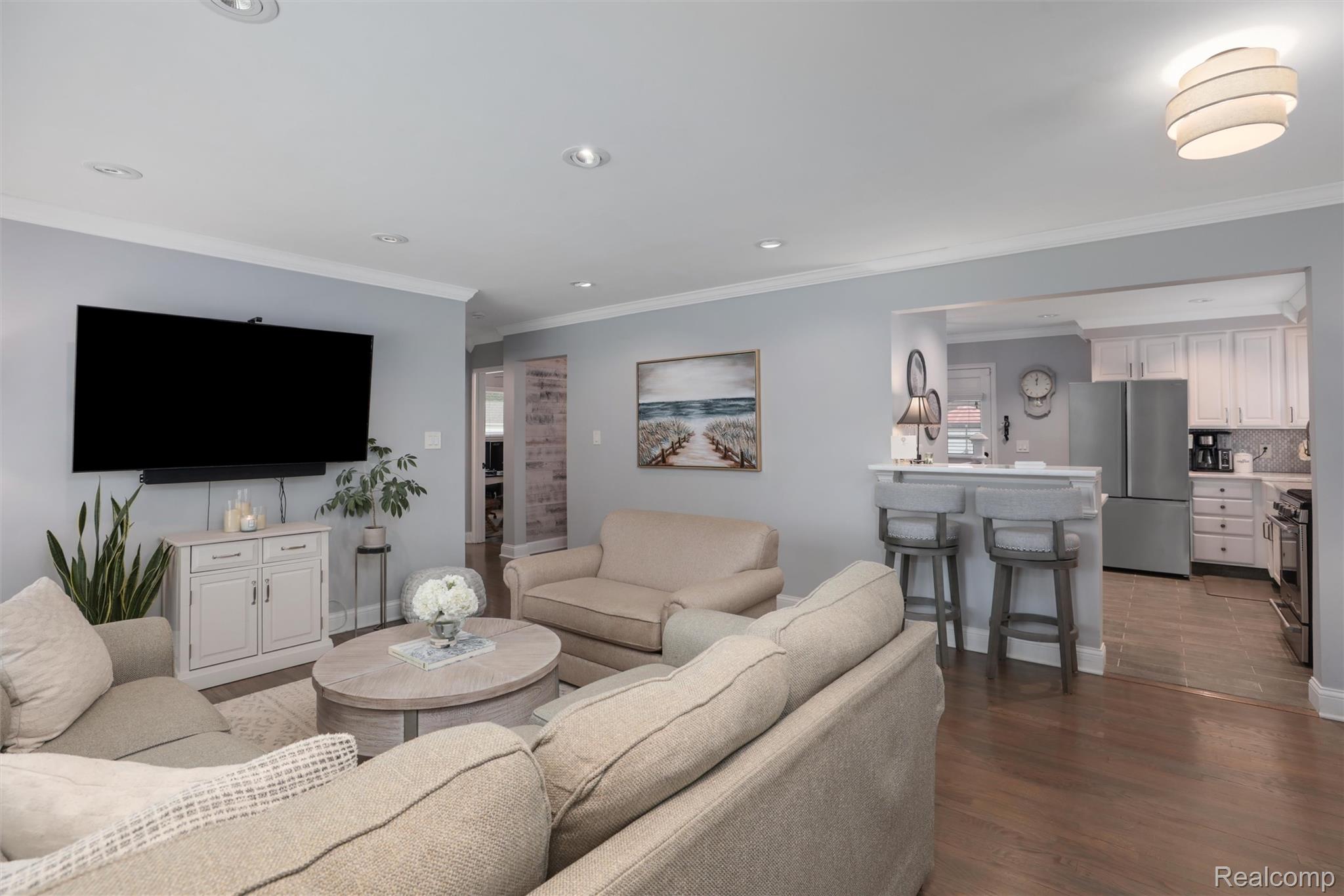 Open-plan living room with beige sofas and a breakfast bar leading to a white kitchen.