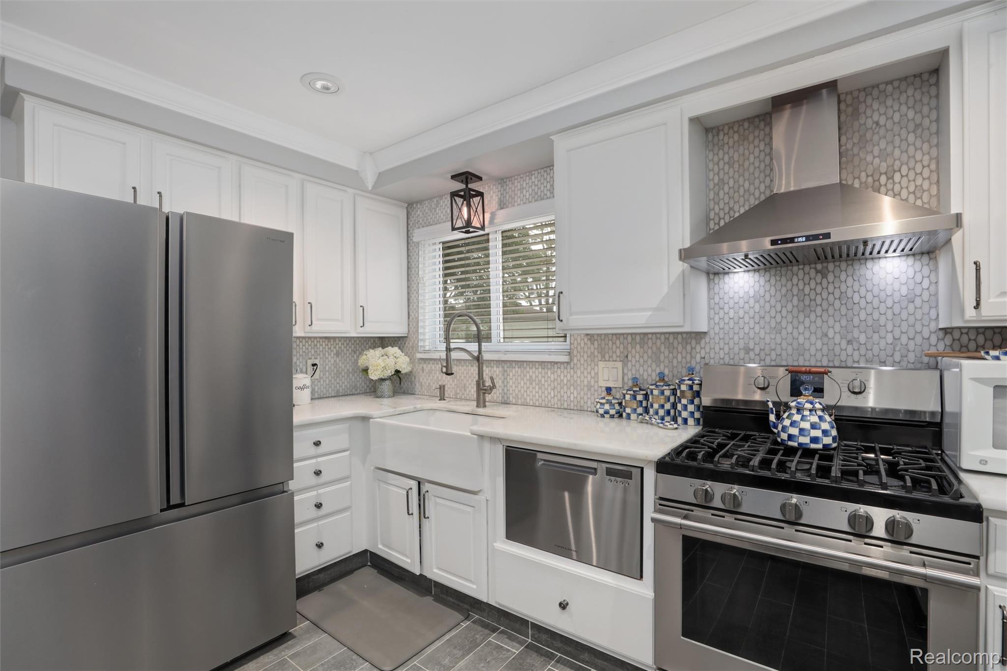 Bright white kitchen with stainless steel appliances, patterned tile backsplash, farmhouse sink and checkered accessories.